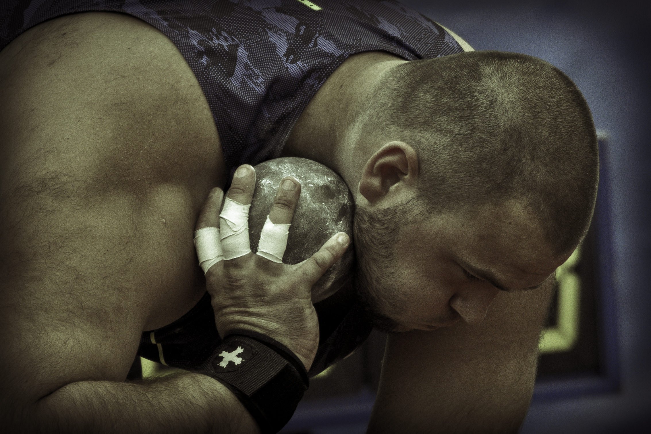 Young male athlete resting after a workout, shirtless with a shaved head, holding a chalk-covered weight or medicine ball.
