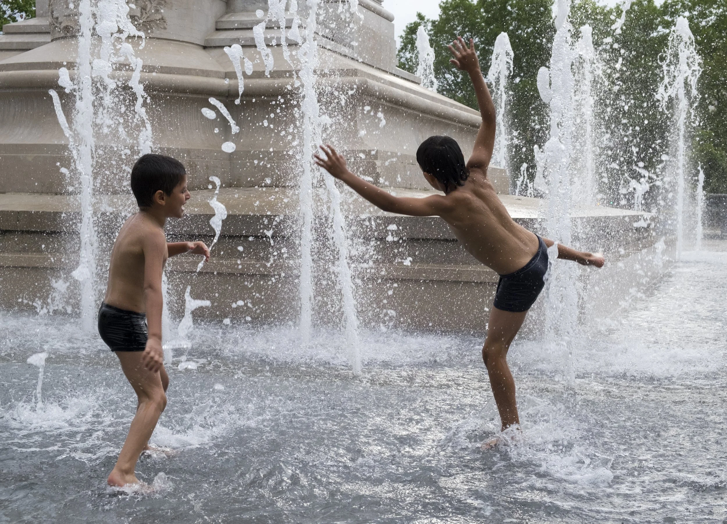 Two children playing in a water fountain, splashing and having fun.