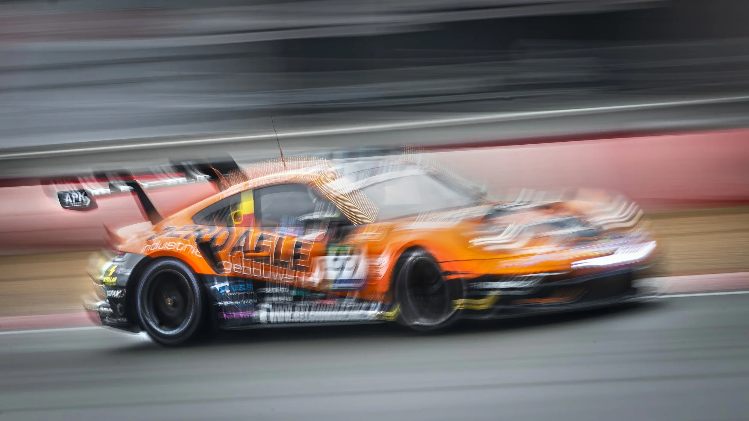 A blurred orange race car with various sponsor logos speeding on a track.