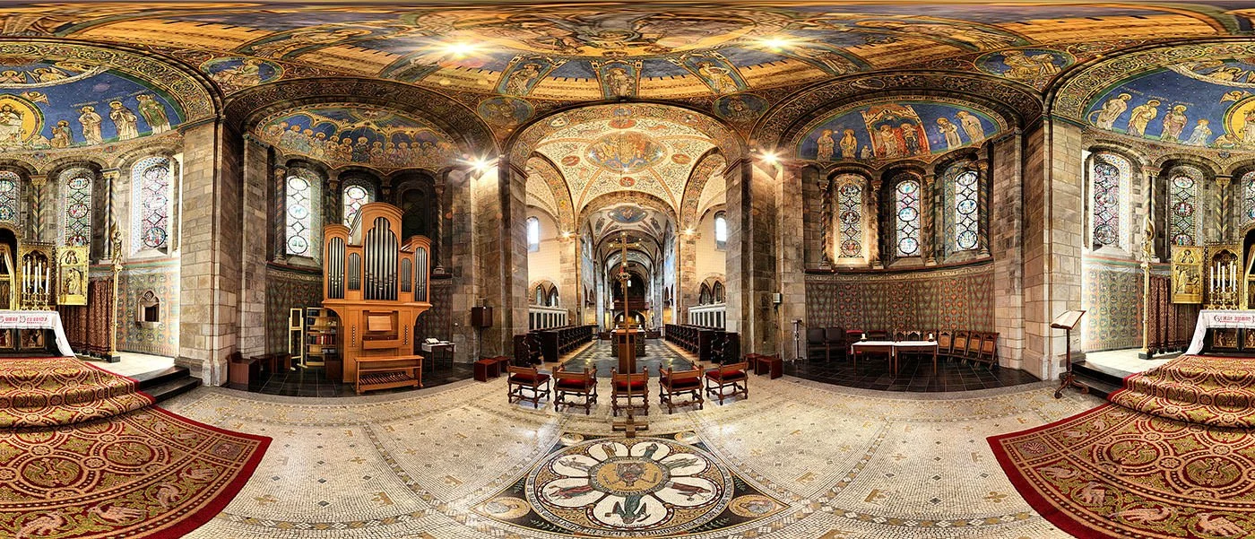 Interior of a church with stained glass windows, ornate ceiling paintings, an organ, altar, and pews.