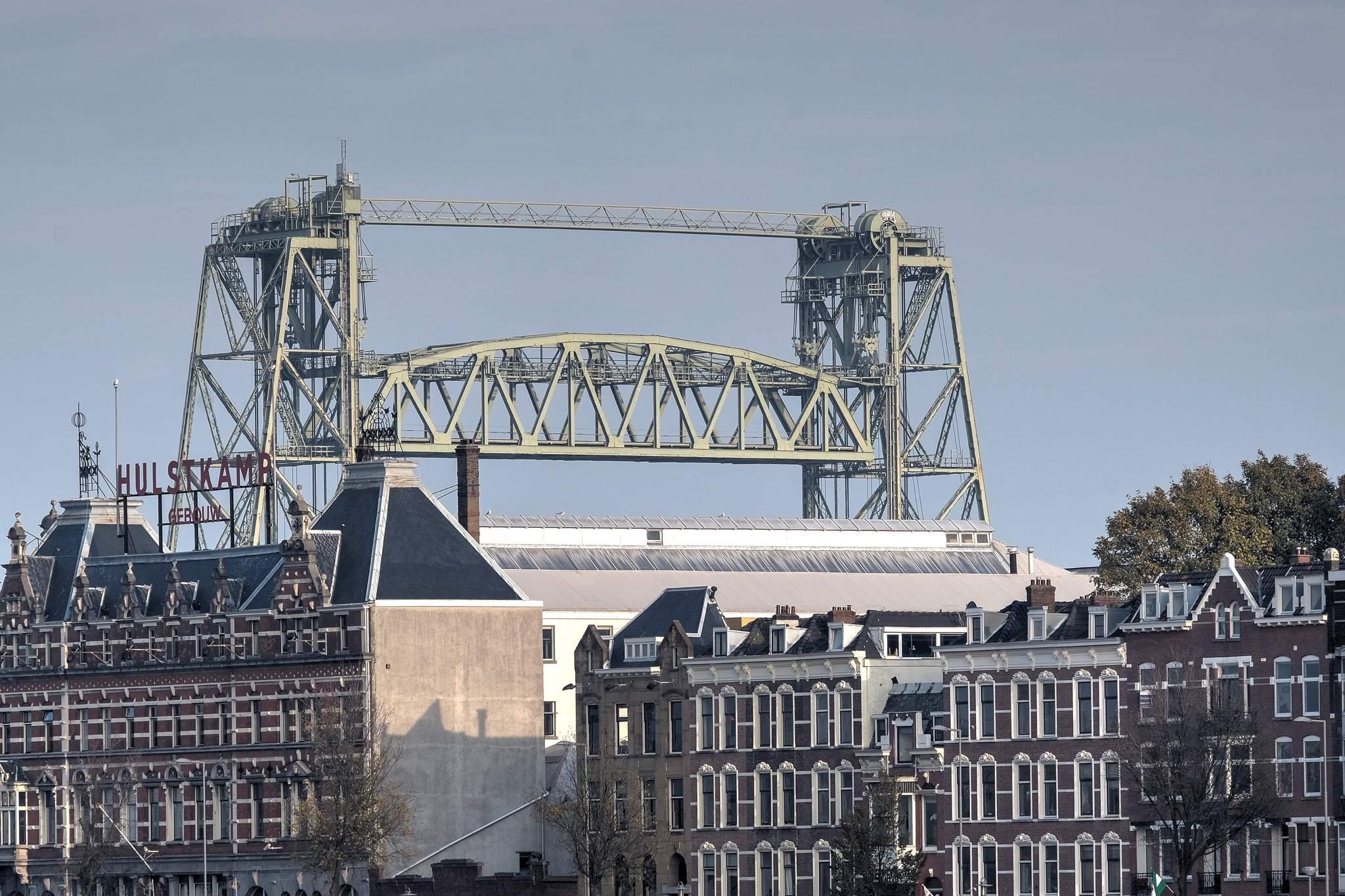 Historical buildings with ornate facades and a large industrial hospital crane in the background, with the sign "HULSKAMP" visible on one of the buildings.