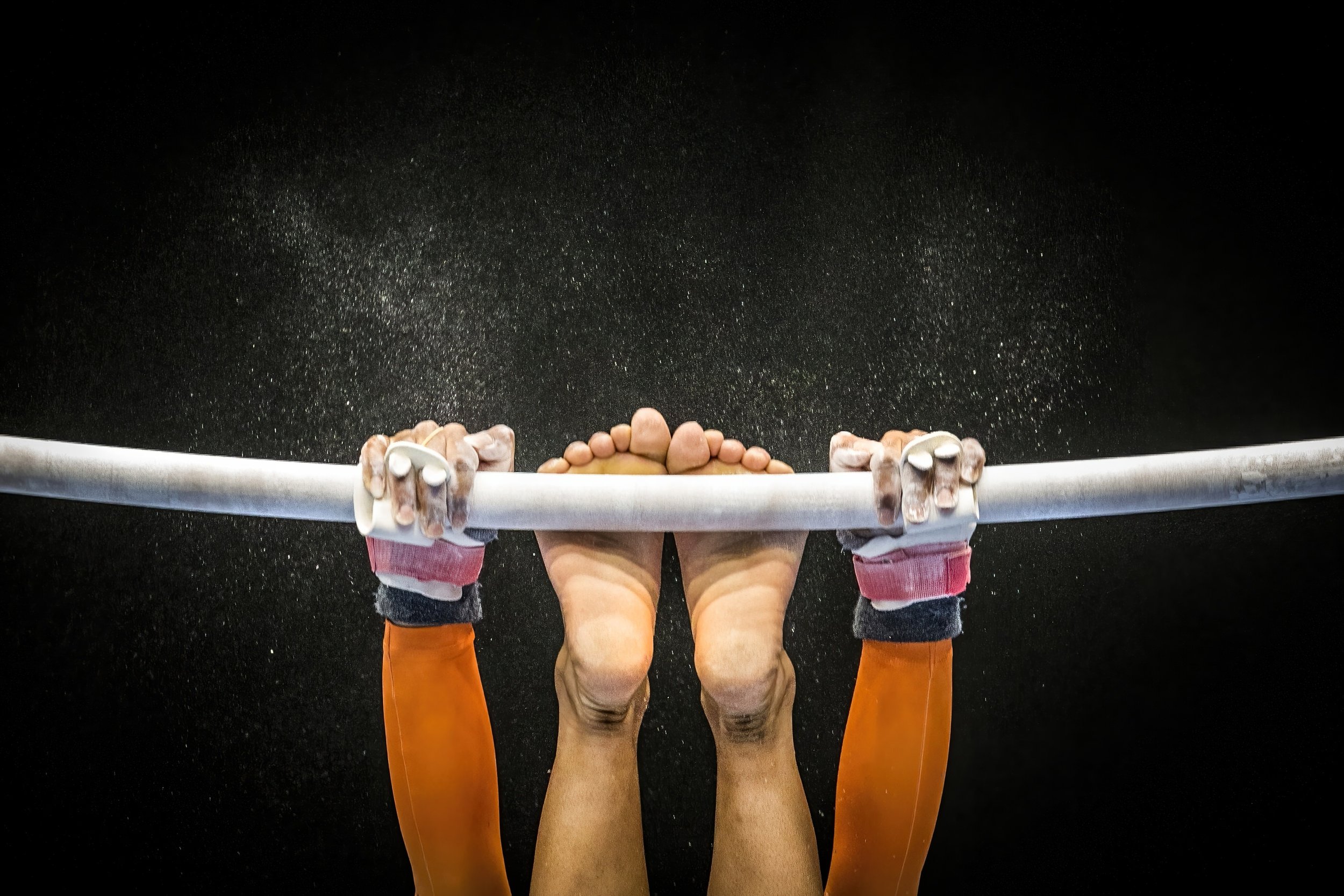 Multiple people holding onto a horizontal bar, seen from below, with a dark background and small particles or dust in the air.