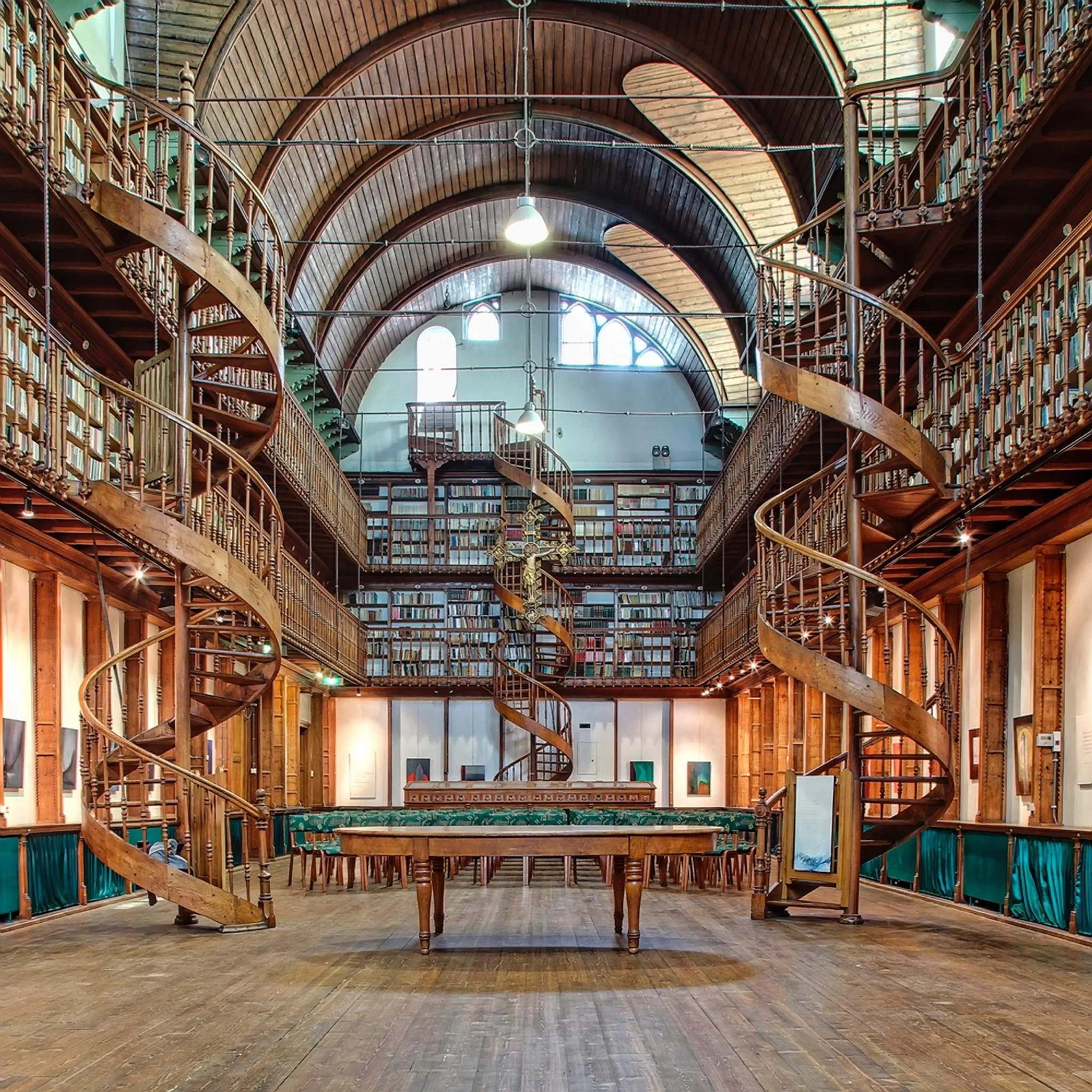 Interior of a multi-level library with wooden bookshelves, spiral staircases, and arched ceilings with large windows.