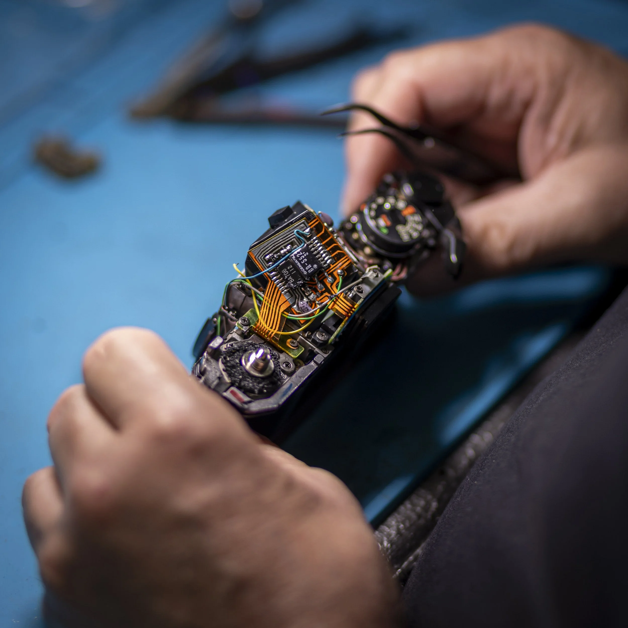 Close-up of a person's hand holding a small electronic circuit board with wires connected, with a blurred background.