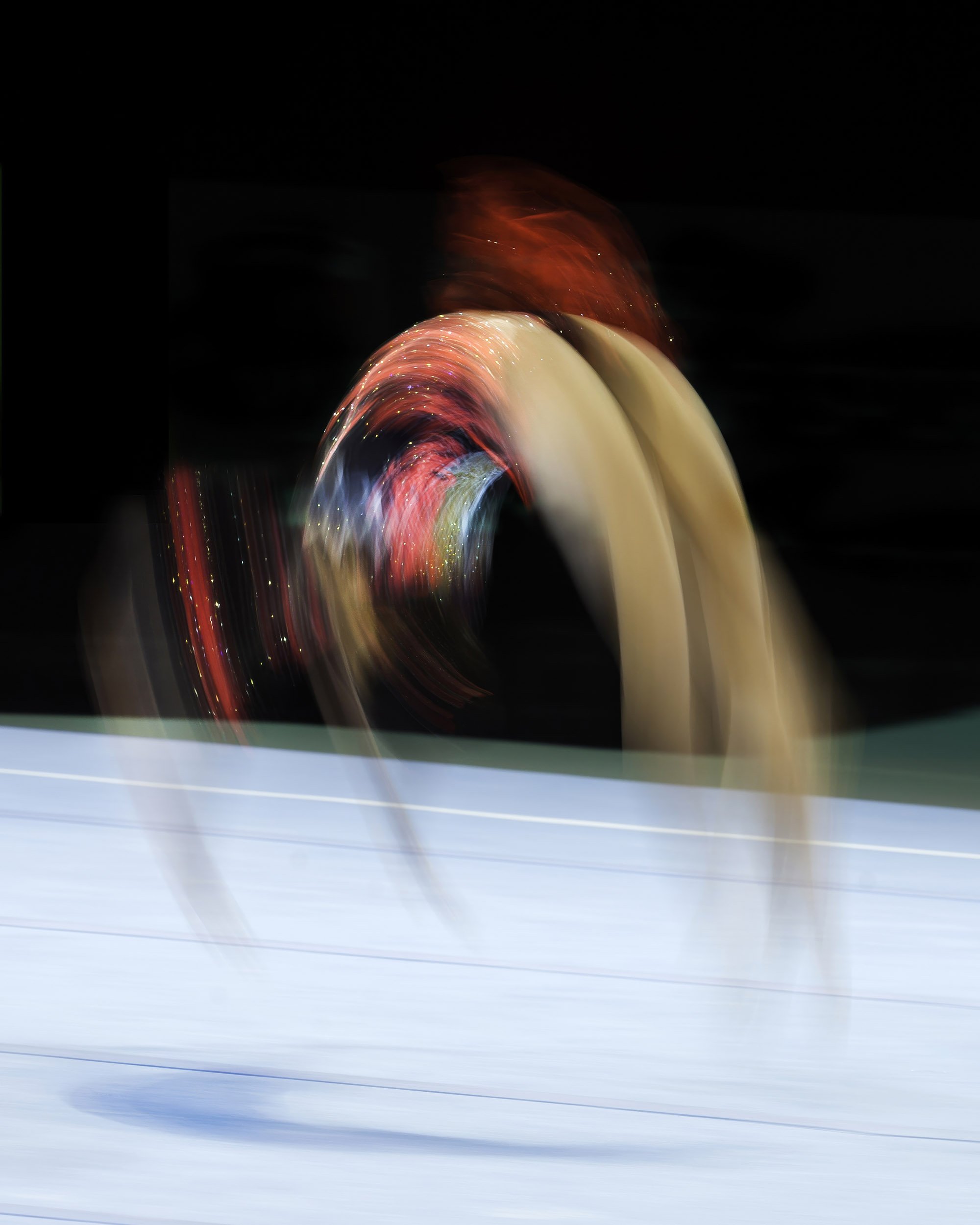 Light trails and streaks of red, blue, and cream colors on a dark background in a long exposure photograph.