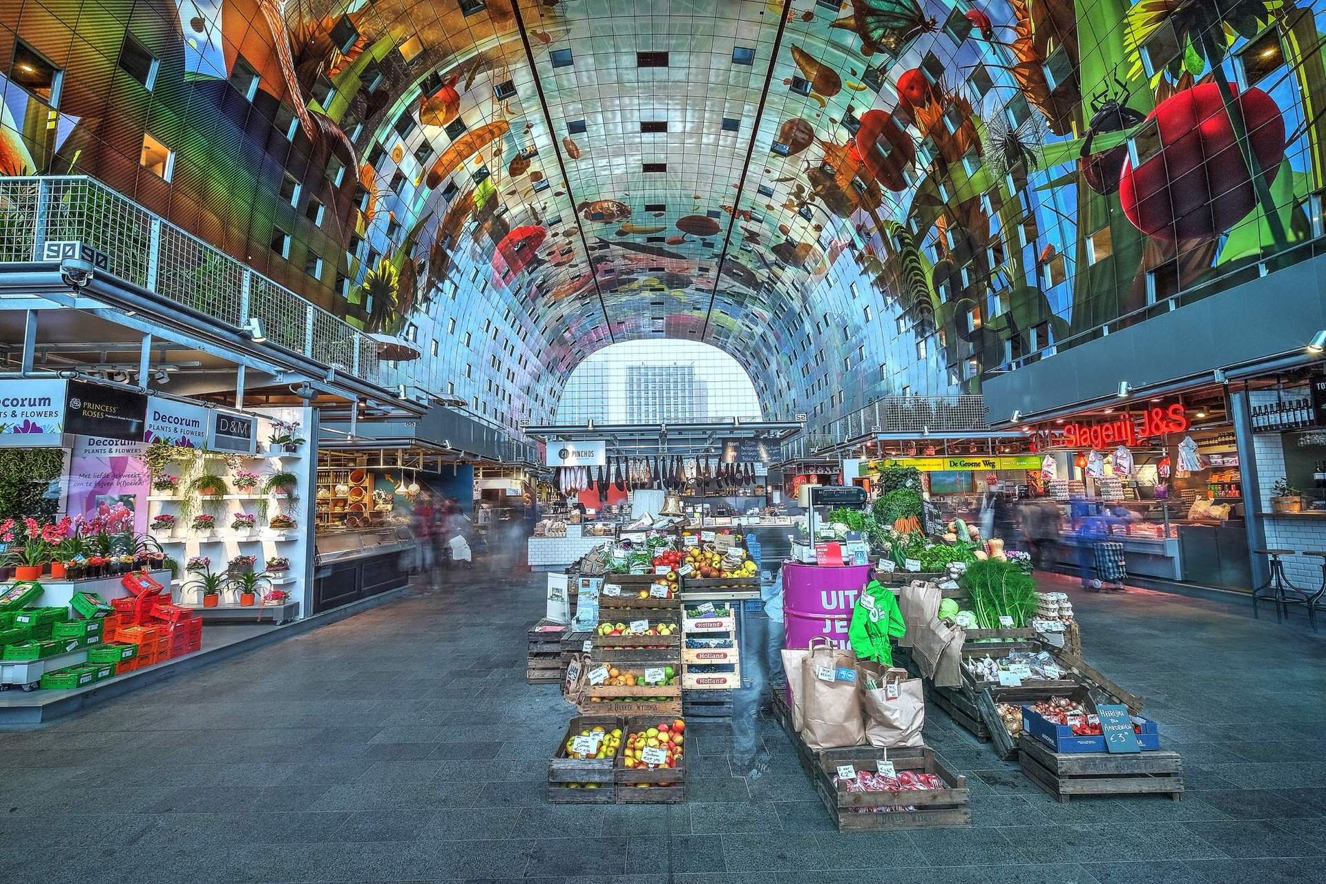 Interior of a vibrant supermarket with a high, arched, colorful mirrored ceiling, displaying reflected images of fruits and vegetables, with various produce stands and grocery items in the foreground.
