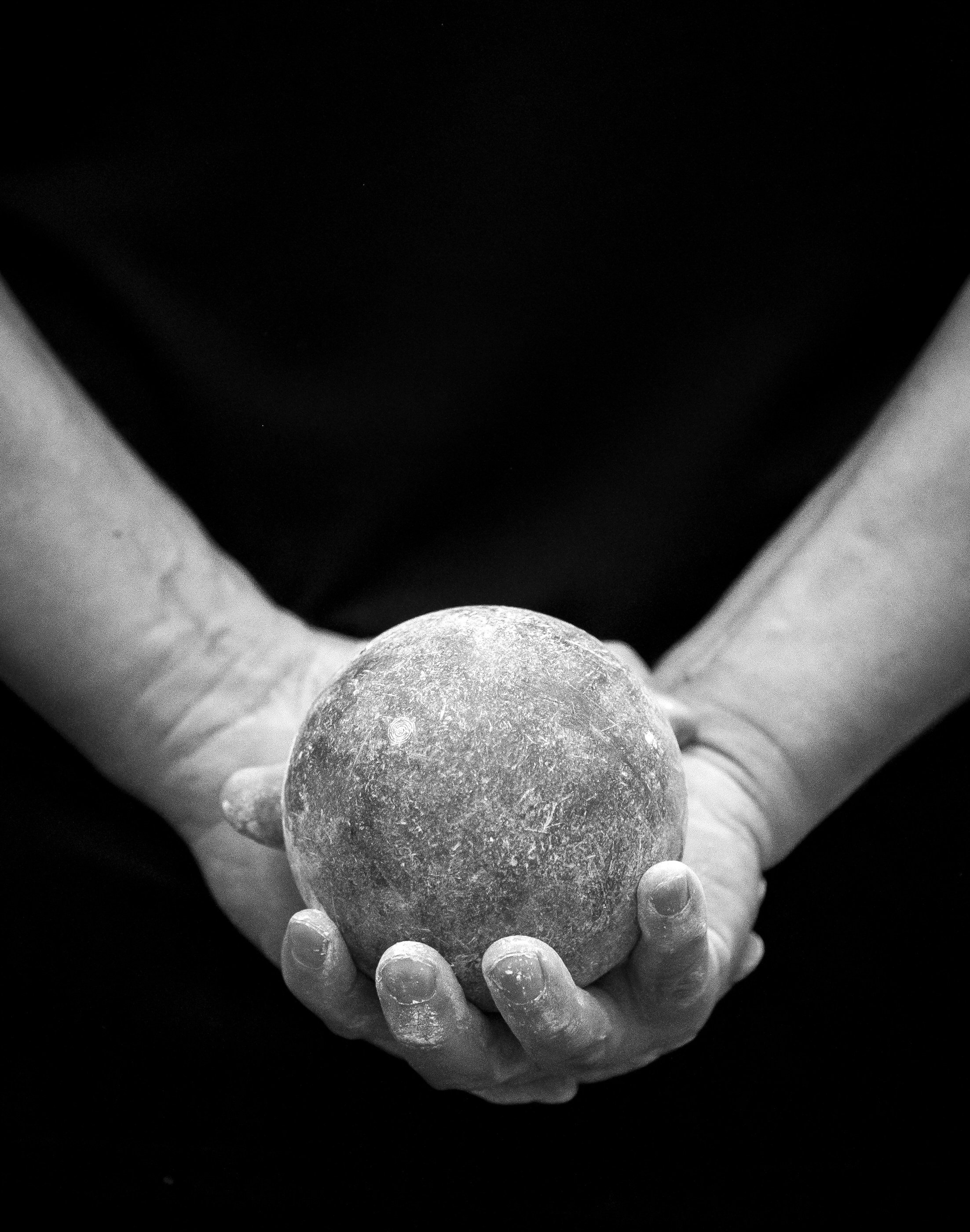 Black and white photo of a person's hand holding a sphere with a textured surface, with smaller spheres surrounding it against a dark background.
