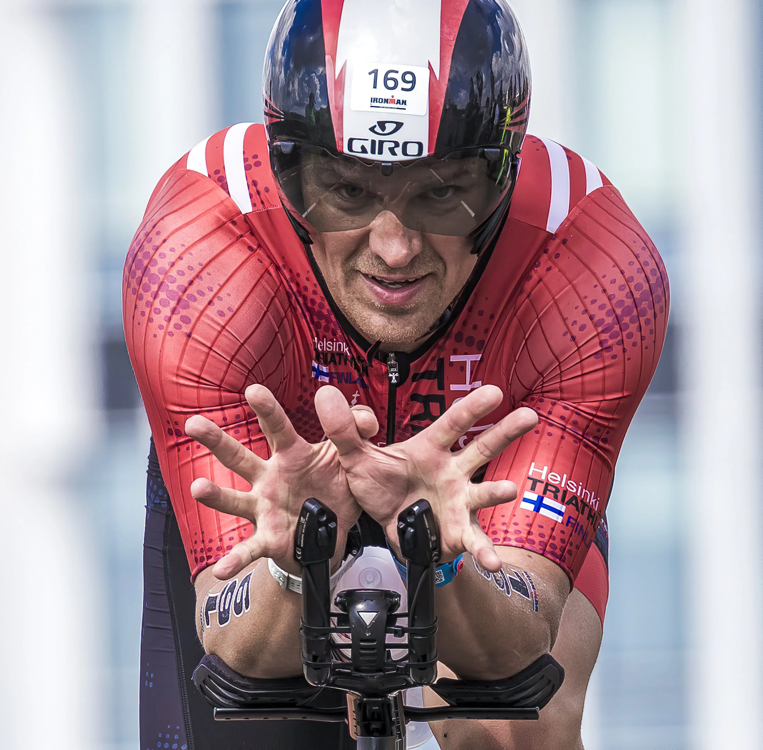 Close-up of a male cyclist wearing a helmet and red jersey, leaning forward with intense focus during a race.