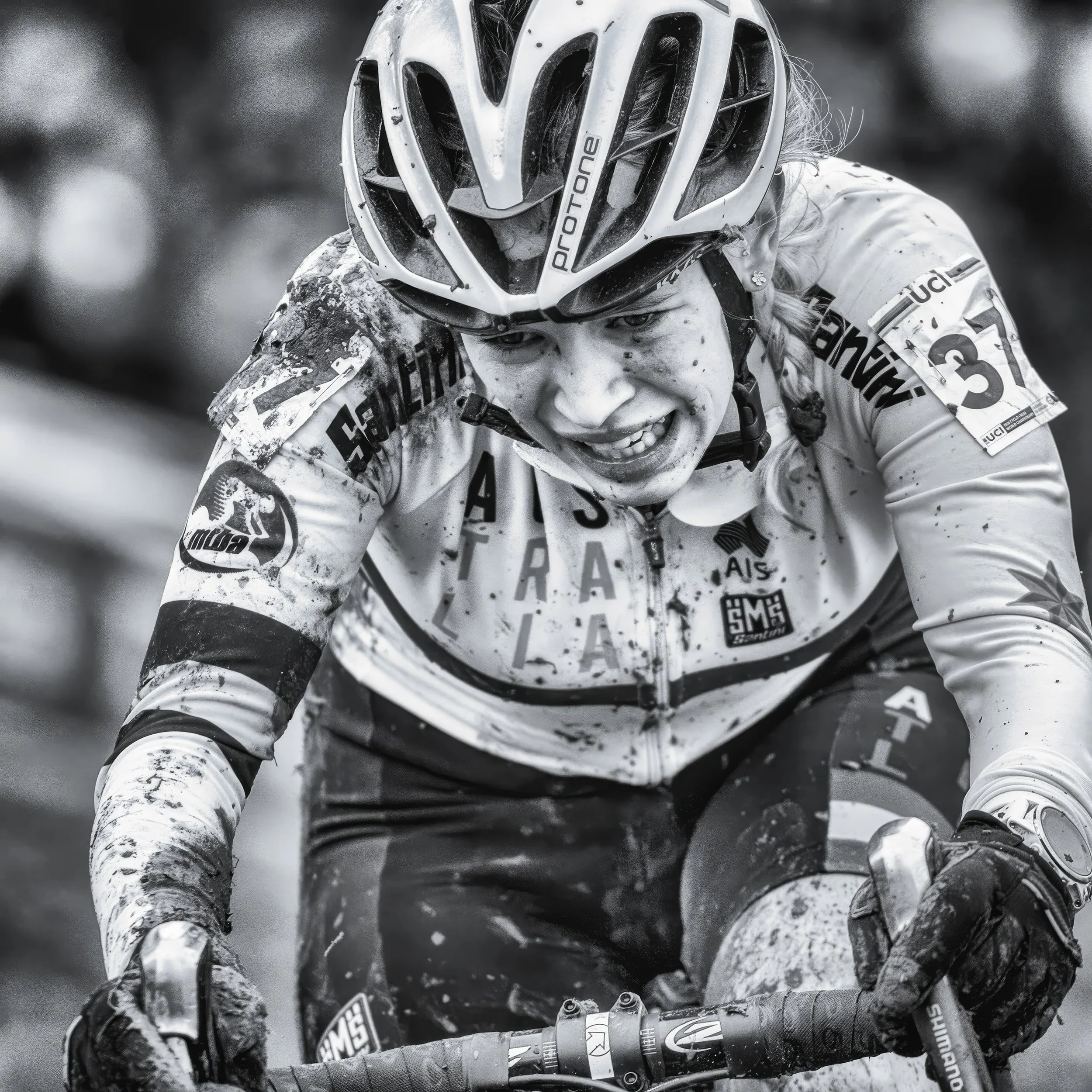 A female cyclist wearing a helmet and sports gear during a competitive race, with the number 13 on her jersey, showing intense focus and effort.