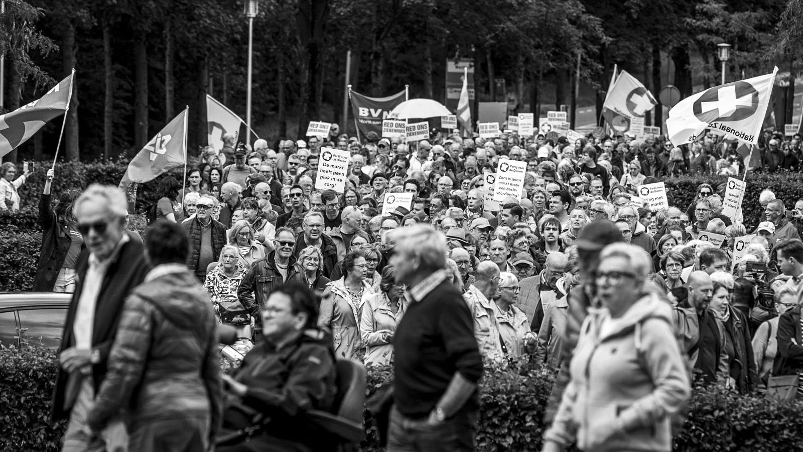 A black and white photo of a large crowd of people participating in a protest or demonstration, holding flags and signs.