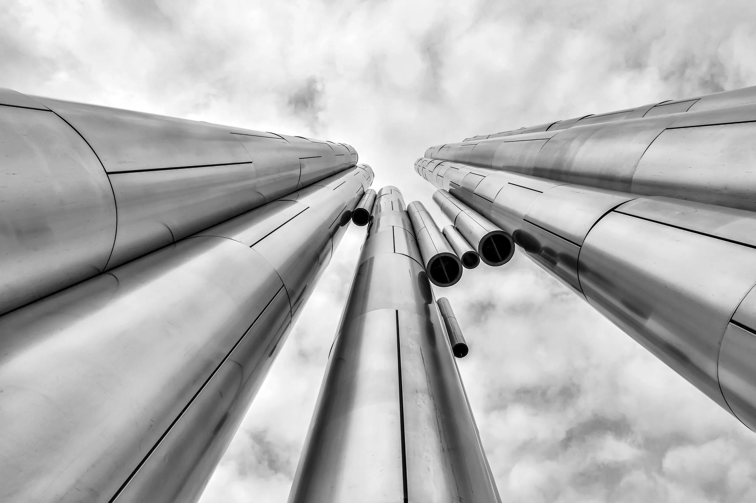 Low-angle view of tall metallic pipes reaching towards a cloudy sky.