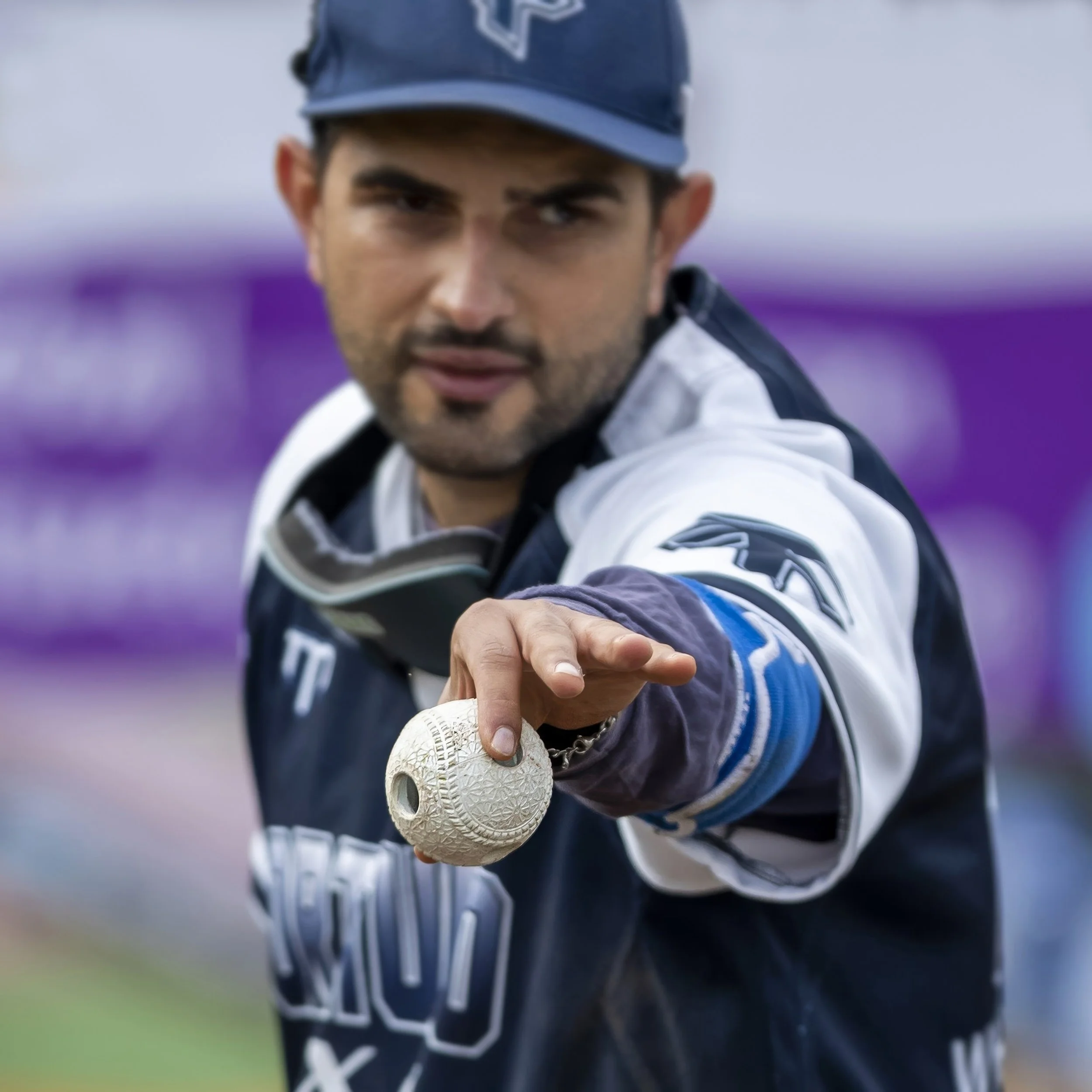 Close-up of a male golfer holding a golf ball close to the camera, wearing a golf cap and sports attire.