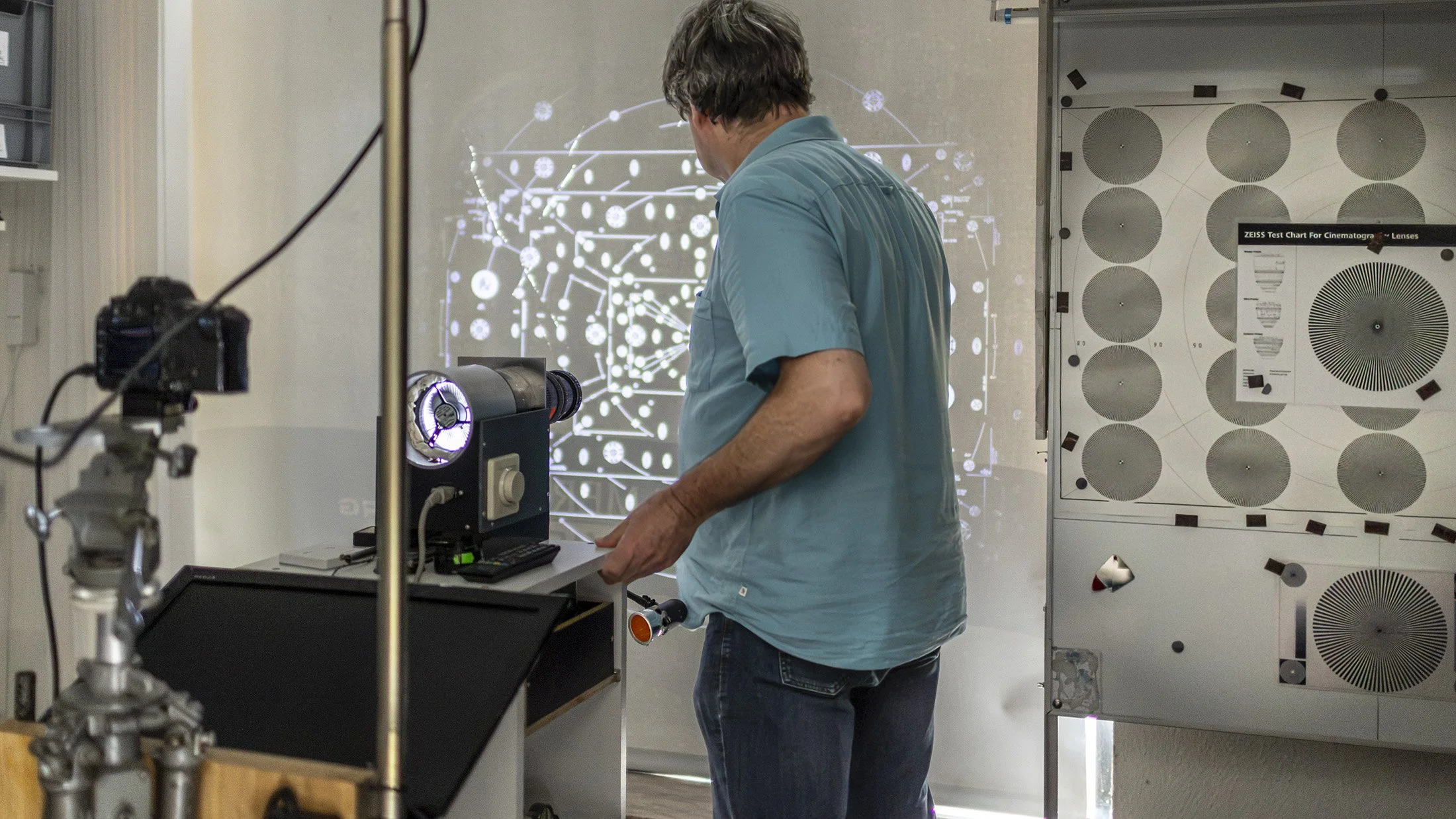 A man in a blue shirt working with scientific equipment in a laboratory, with a digital projection of a neural network or complex data visualization in the background.