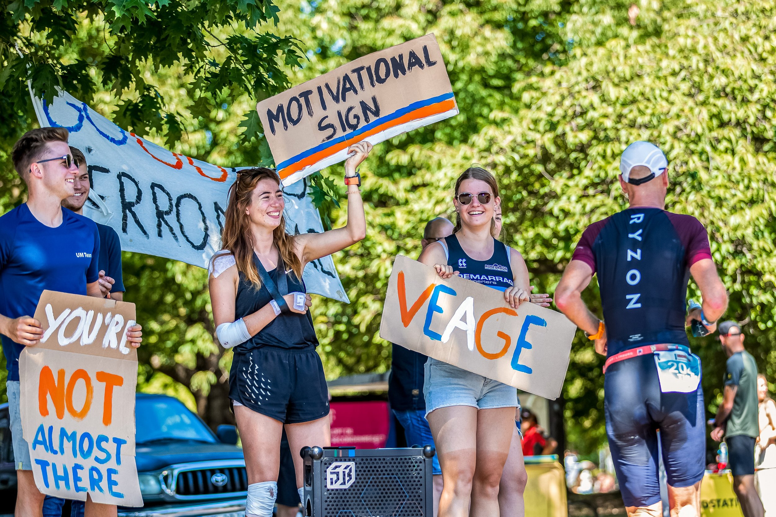 Group of people participating in a protest or rally, holding signs advocating for climate change awareness and action. The setting is outdoors with green trees in the background.