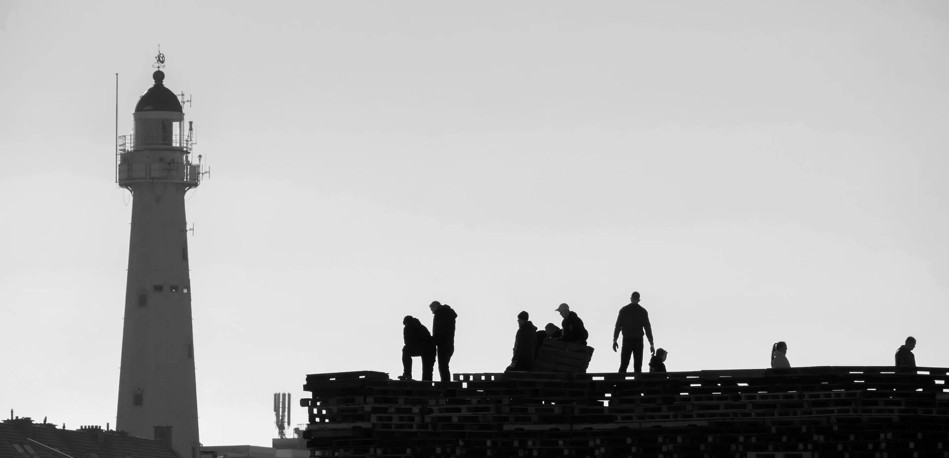 Silhouette of people on a rooftop near a lighthouse