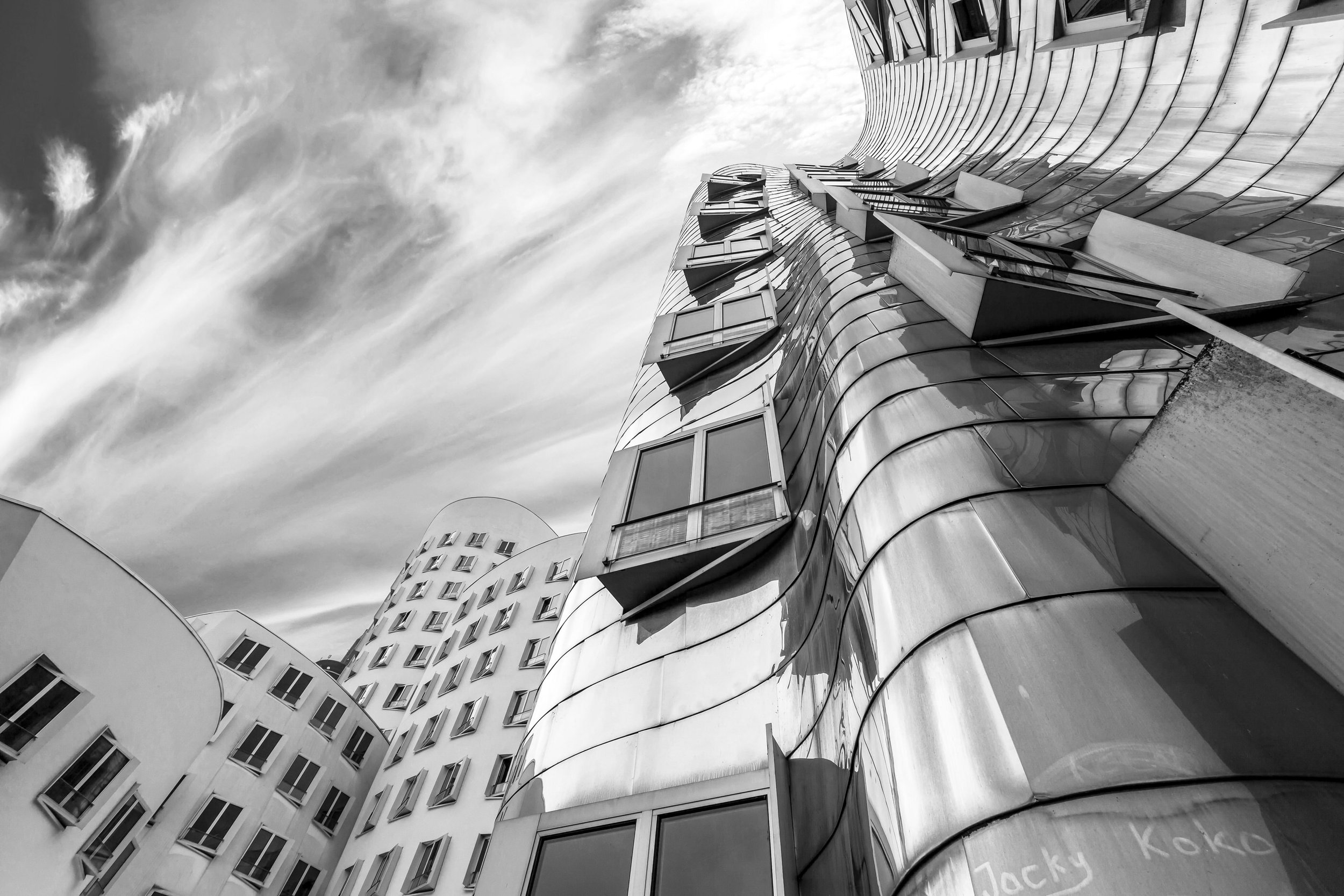 Black and white photo of modern, curved architectural building with reflective glass windows and rounded balconies, under a cloudy sky.
