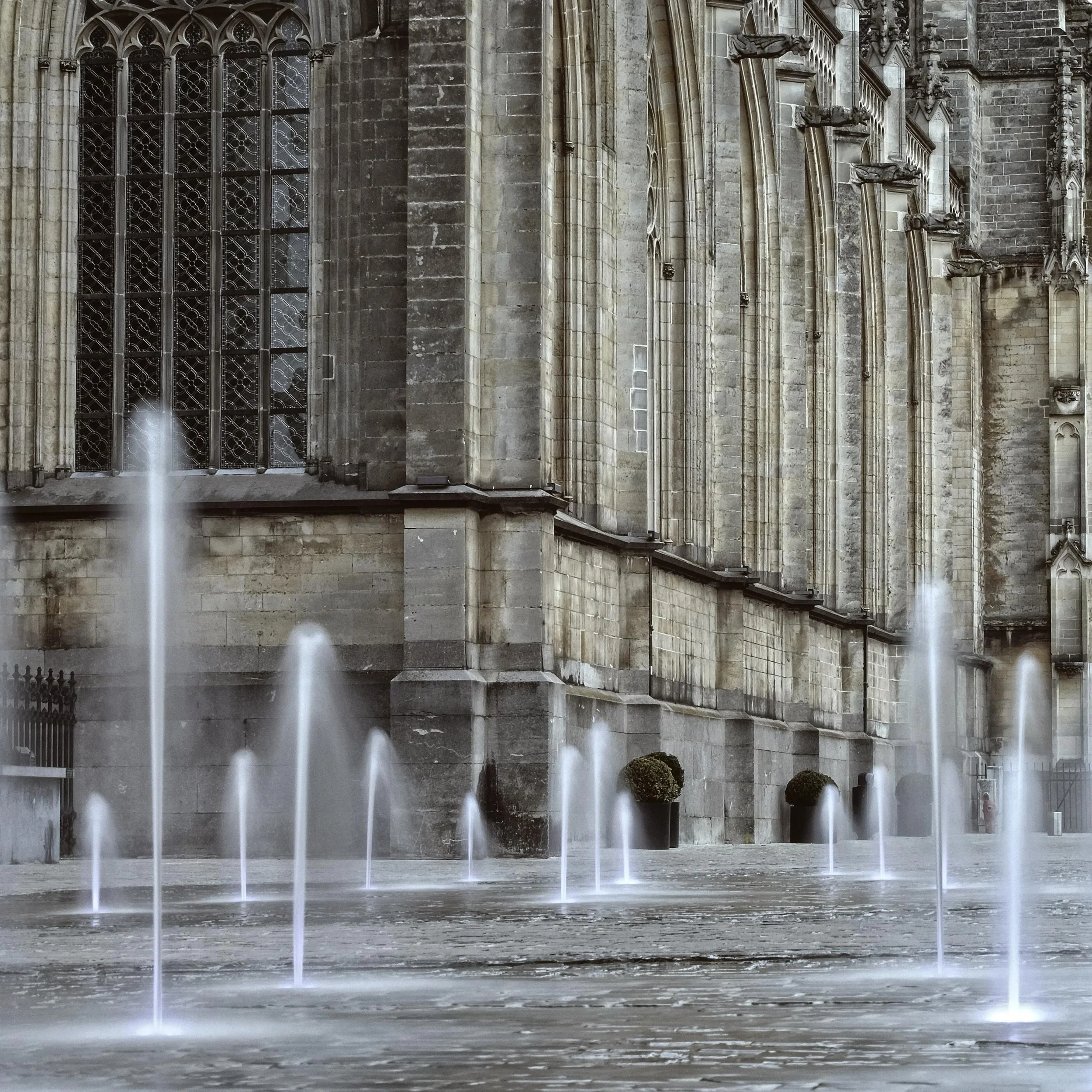 A large Gothic-style cathedral with stained glass windows and flying buttresses, viewed with a fountain in the foreground.