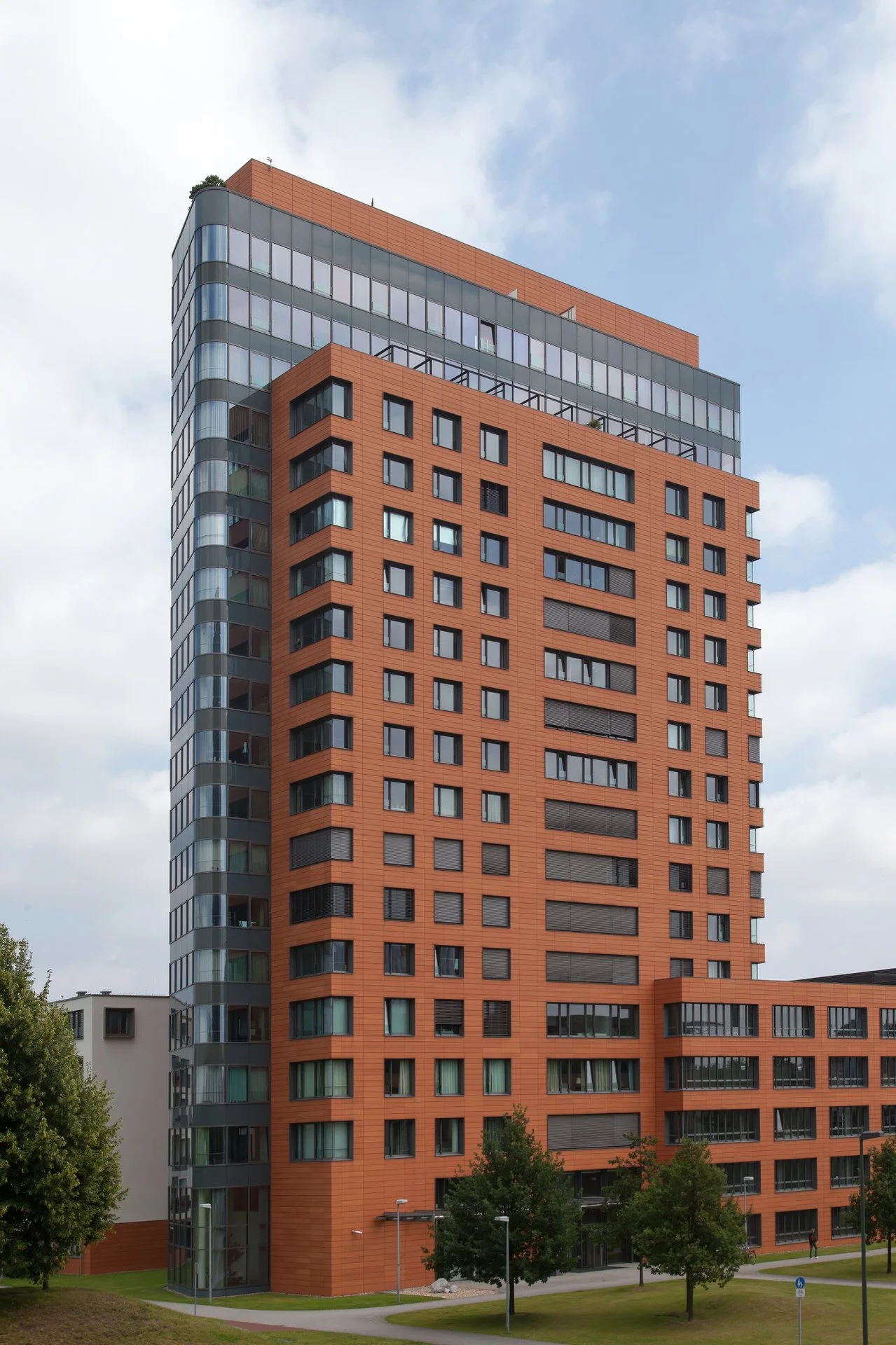 Modern high-rise building with orange and gray facade, glass windows, and trees in front.