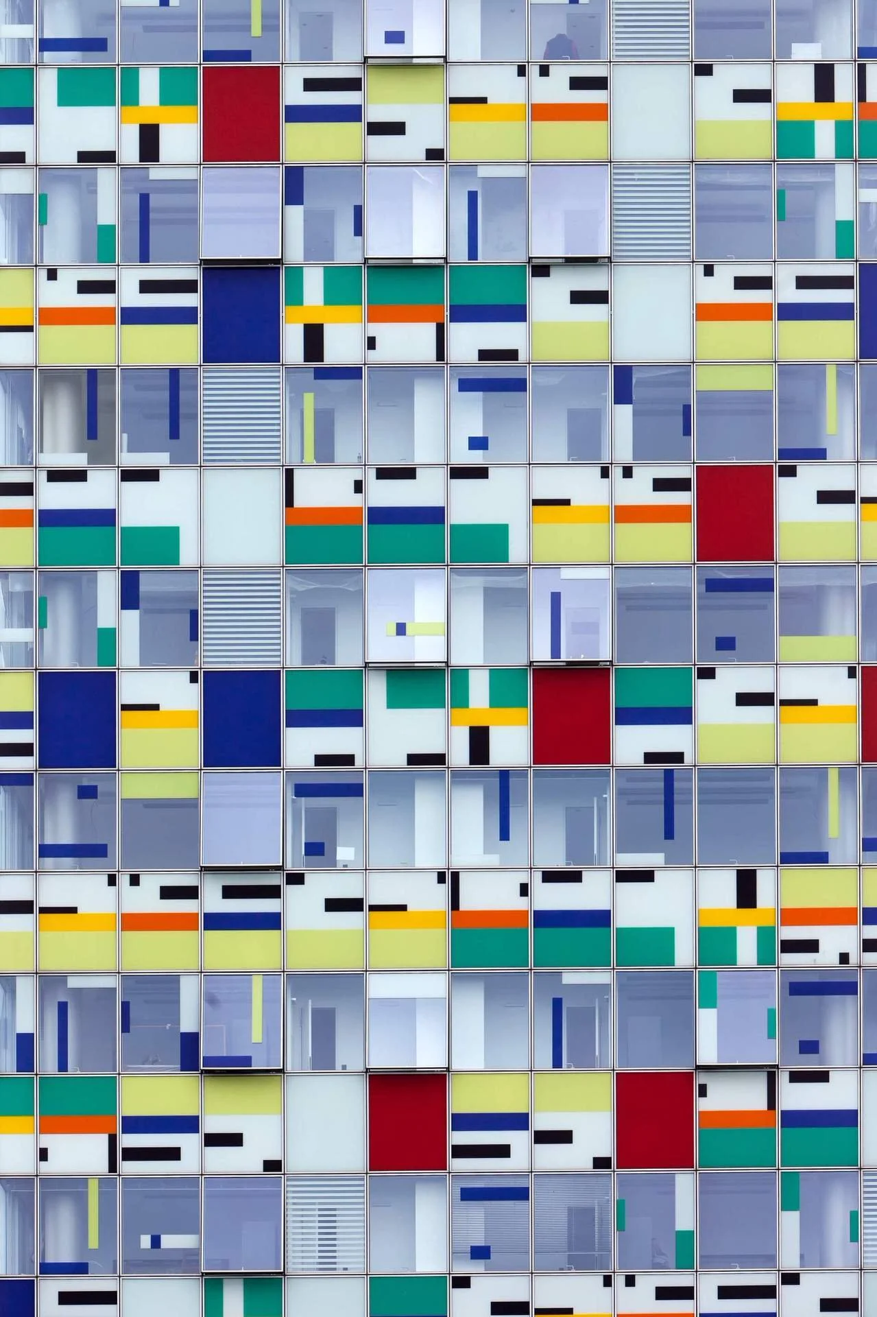 Colorful geometric abstract pattern with grid of small squares in various colors and patterns, including primary and secondary colors, some with stripes or blocks.