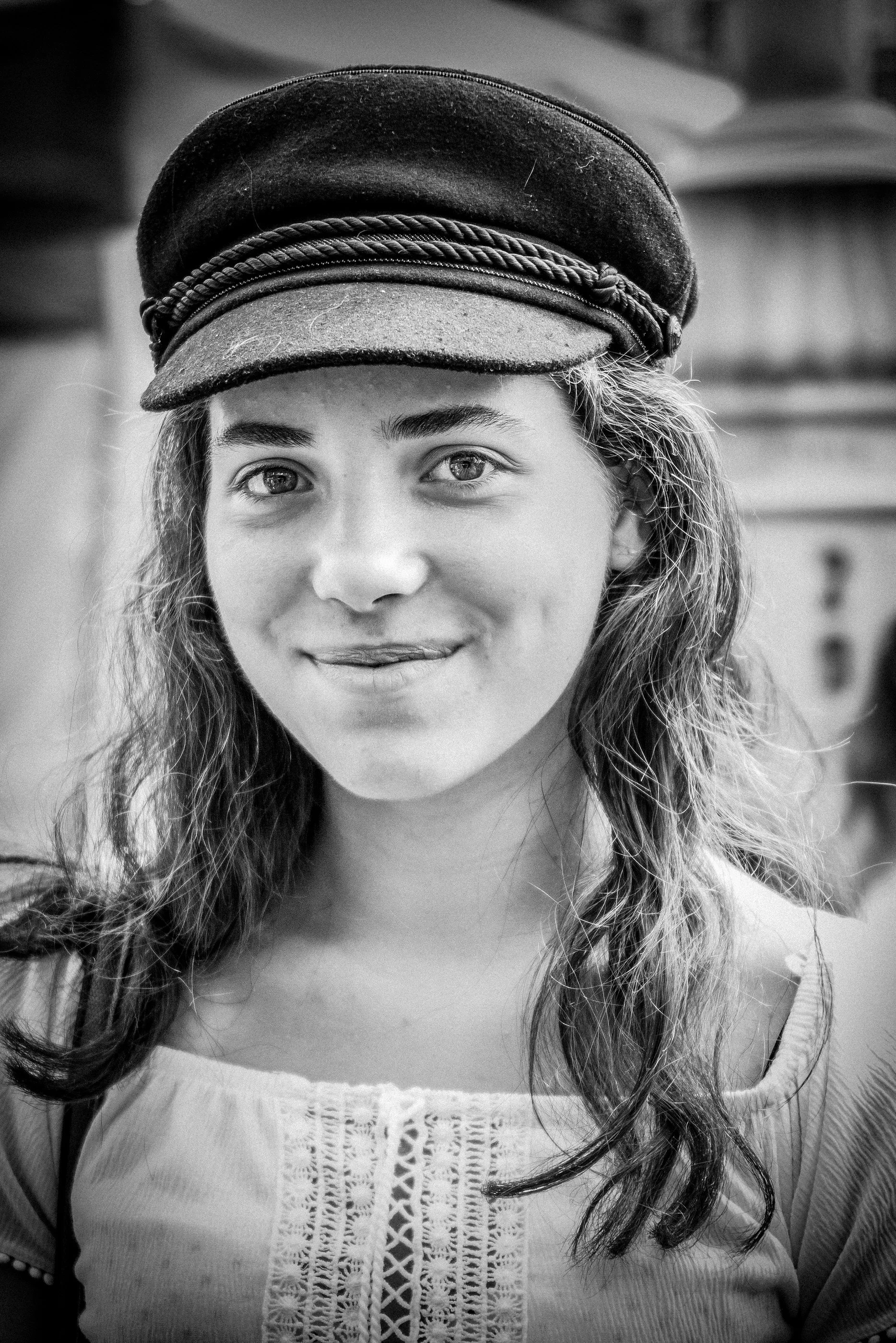 Black and white photo of a young woman wearing a cap and a top with lace details, smiling slightly, with curly hair.
