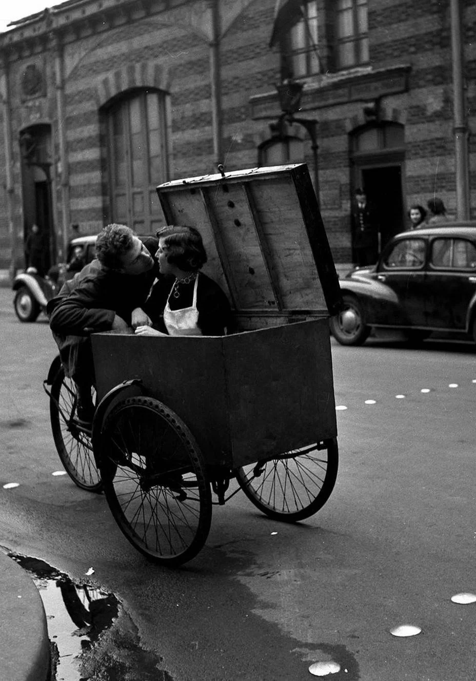 A tender moment of affection discovered in the middle of an ordinary working day. Doisneau turns a simple street scene into a warm and playful observation of love, reminding us that humanity often reveals itself in the most unexpected places.