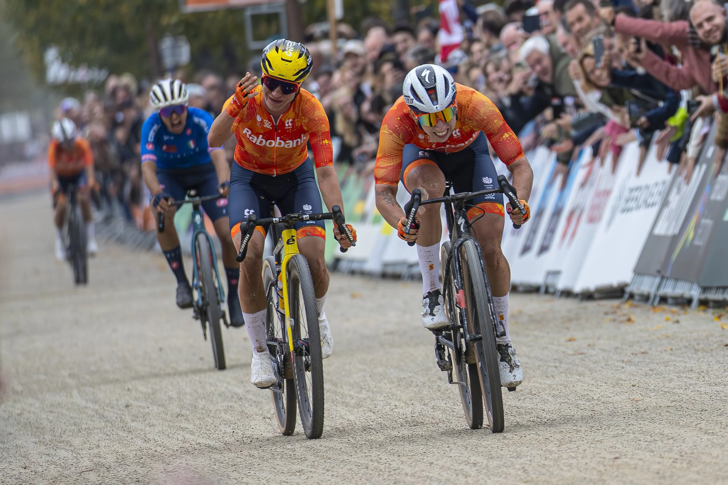 Cyclists participating in a race, wearing colorful jerseys and helmets, with a crowd of spectators cheering behind barriers.