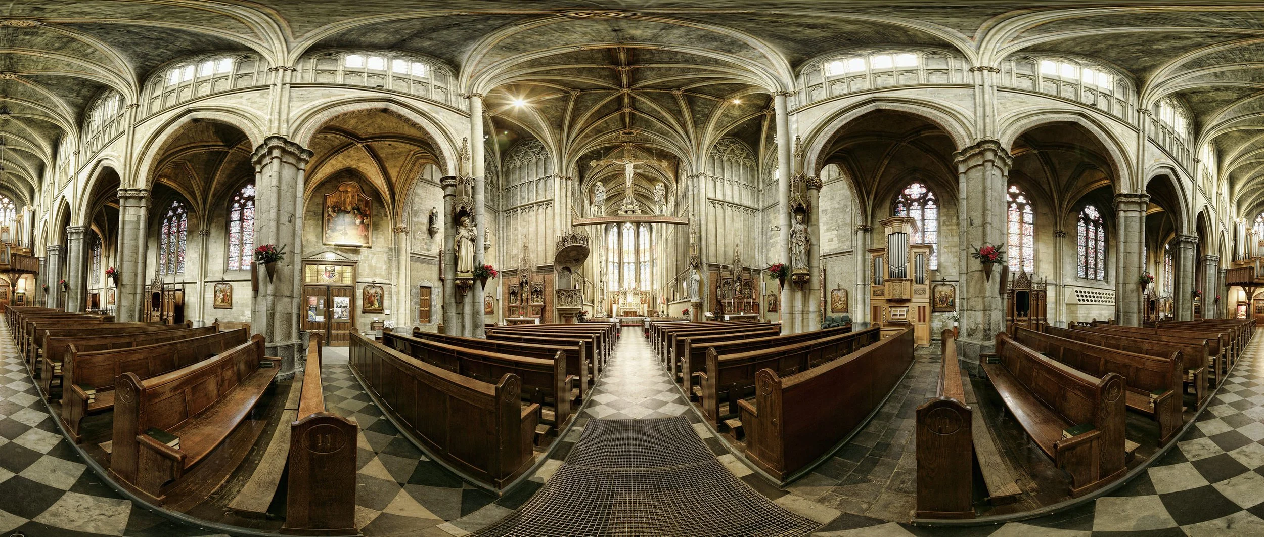 Interior of a Gothic-style church with high vaulted ceilings, stained glass windows, wooden pews, and religious statues.