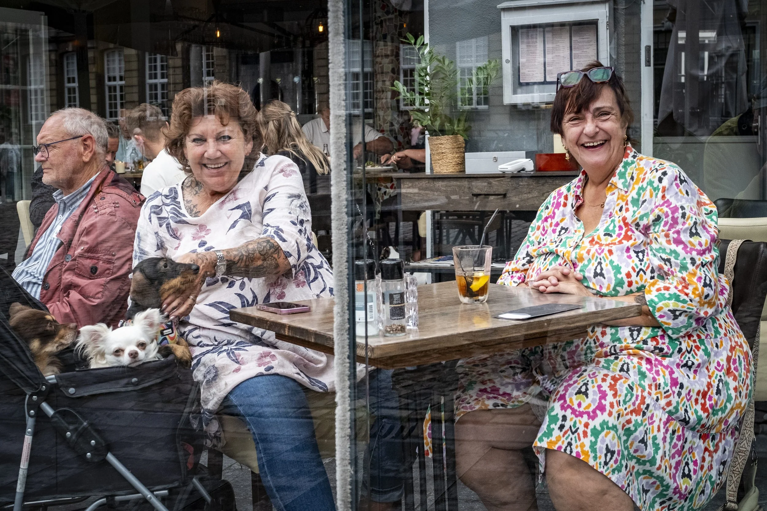 People sitting at a restaurant table, smiling and enjoying themselves, with dogs on their laps.