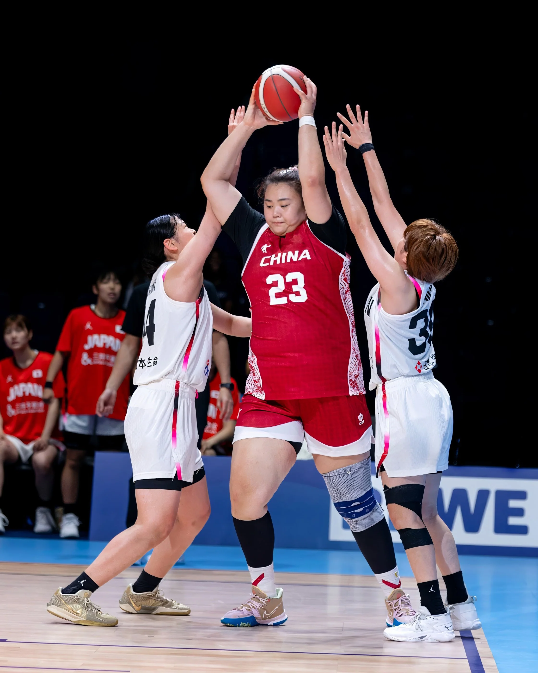 Chinese female volleyball player wearing red jersey number 23 jumping to hit the ball as teammates block