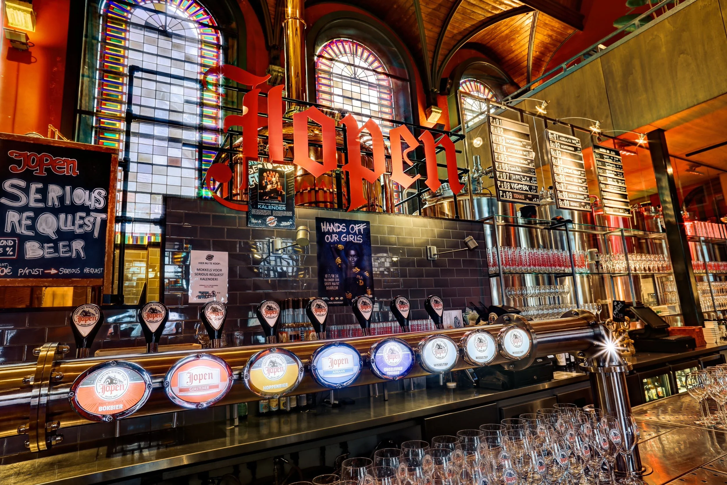 Inside a brewery bar with illuminated stained glass windows, beer taps, chalkboard menu, and decorative signage.