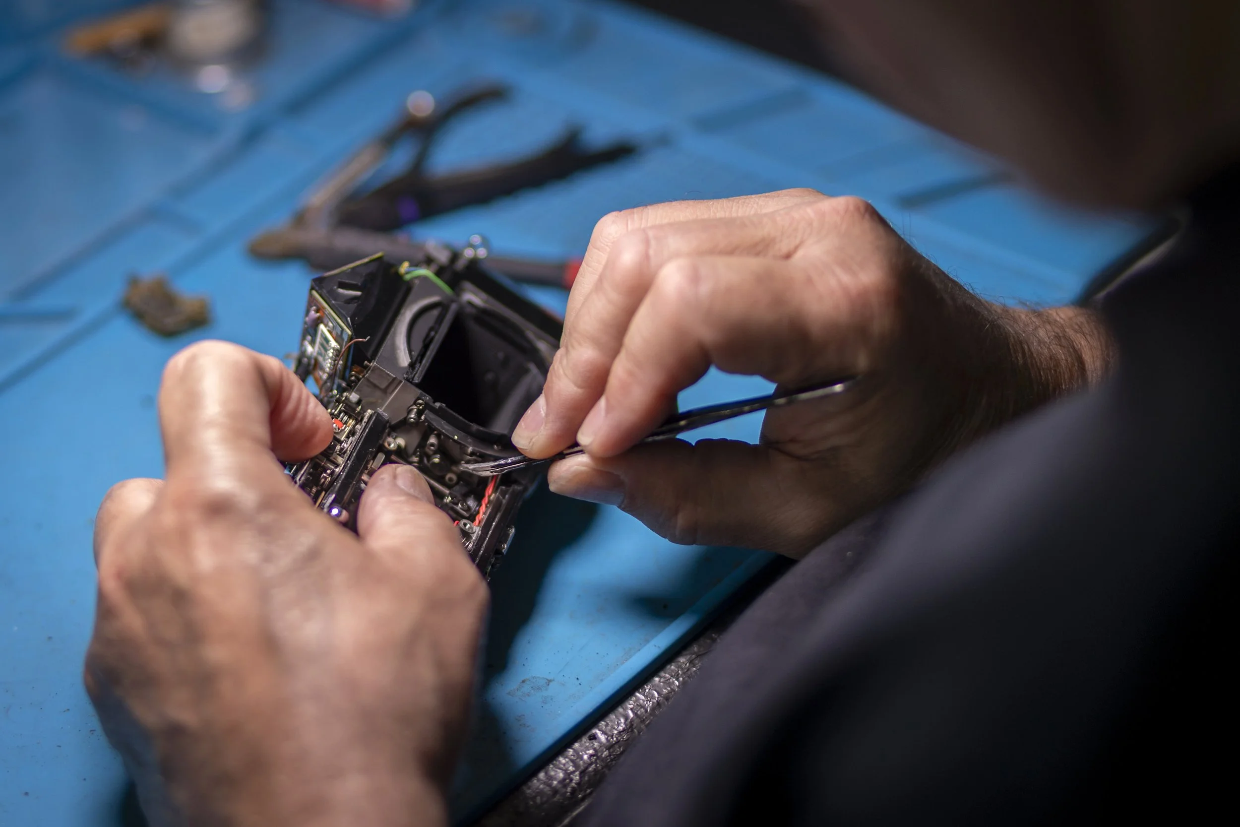 A person working on electronic device components on a blue work surface, with tools in the background.