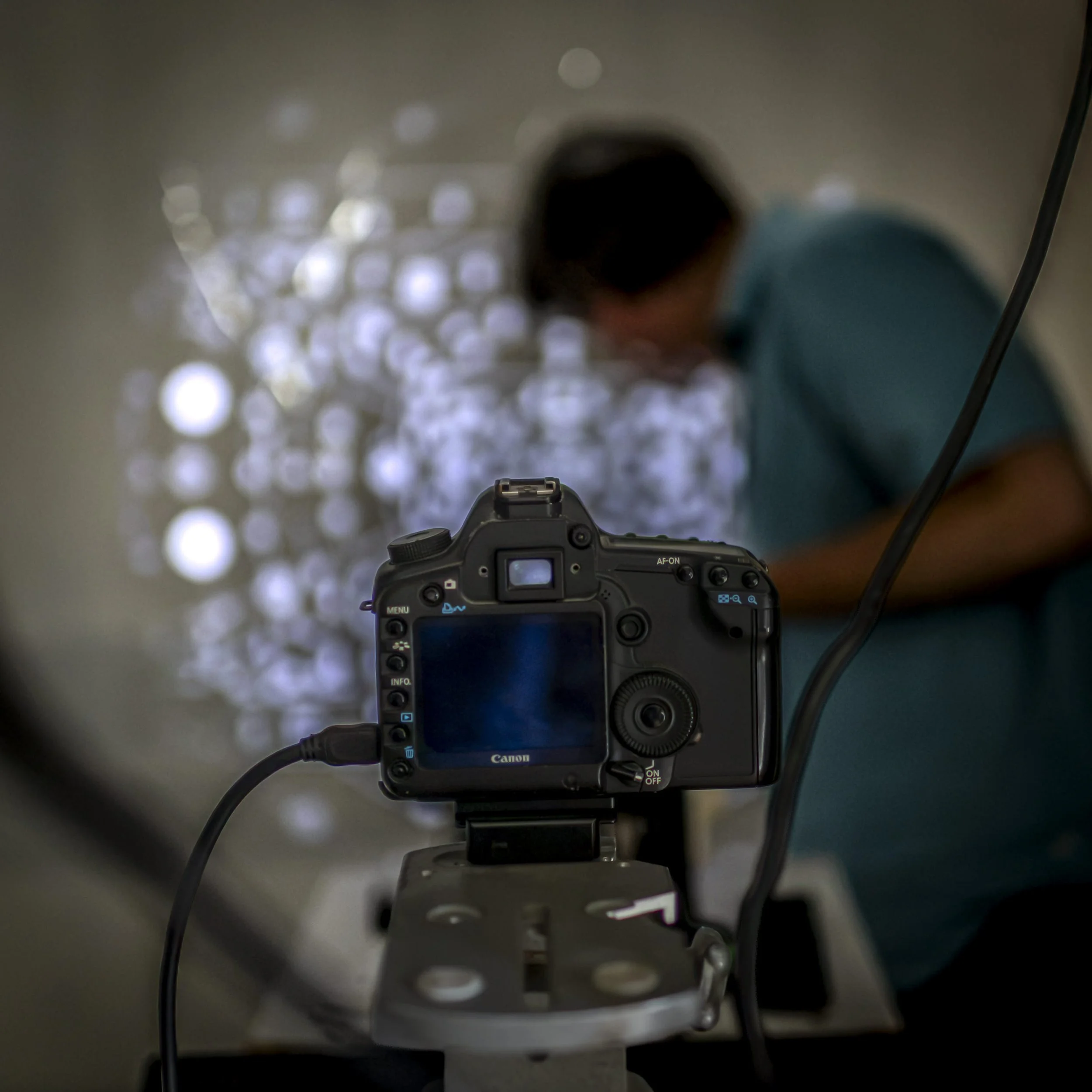 The view of the inside of a camera lens with the camera's LCD screen displaying the scene being captured, including a blurred person in front of a reflective surface with light spots.