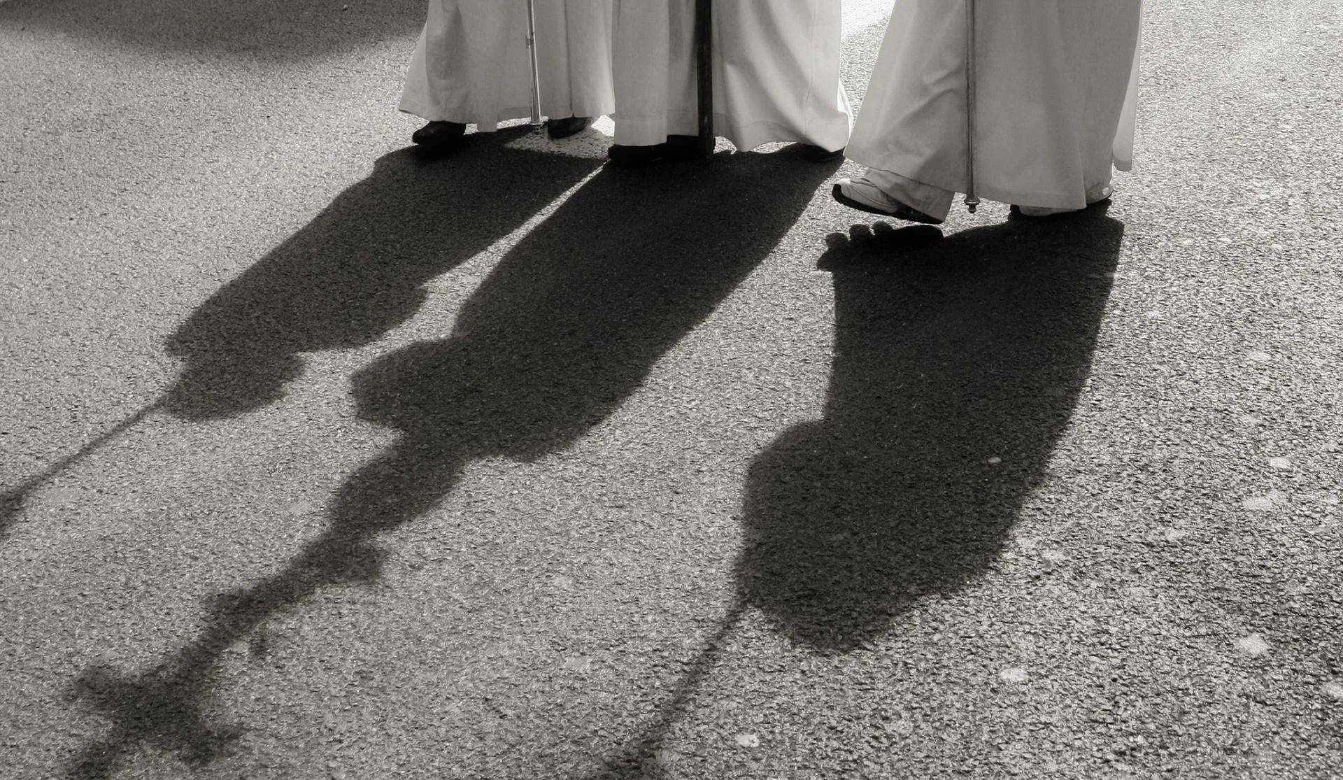 People wearing white robes standing on pavement, casting lengthy shadows.