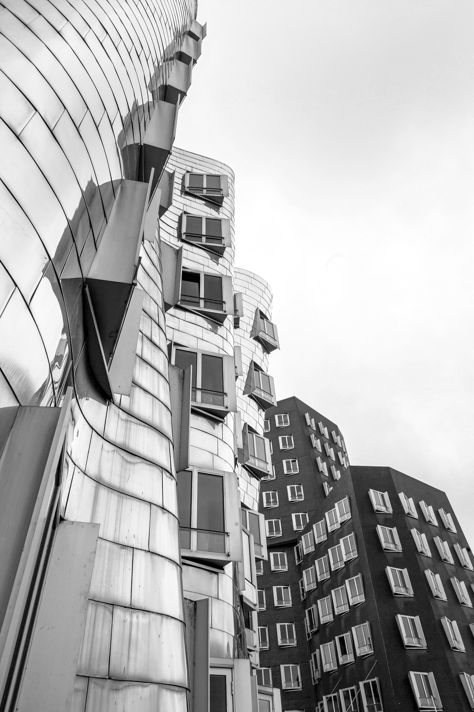 A black-and-white photograph of a modern, curved building with multiple windows and balconies, viewed from a low angle against a mostly clear sky.