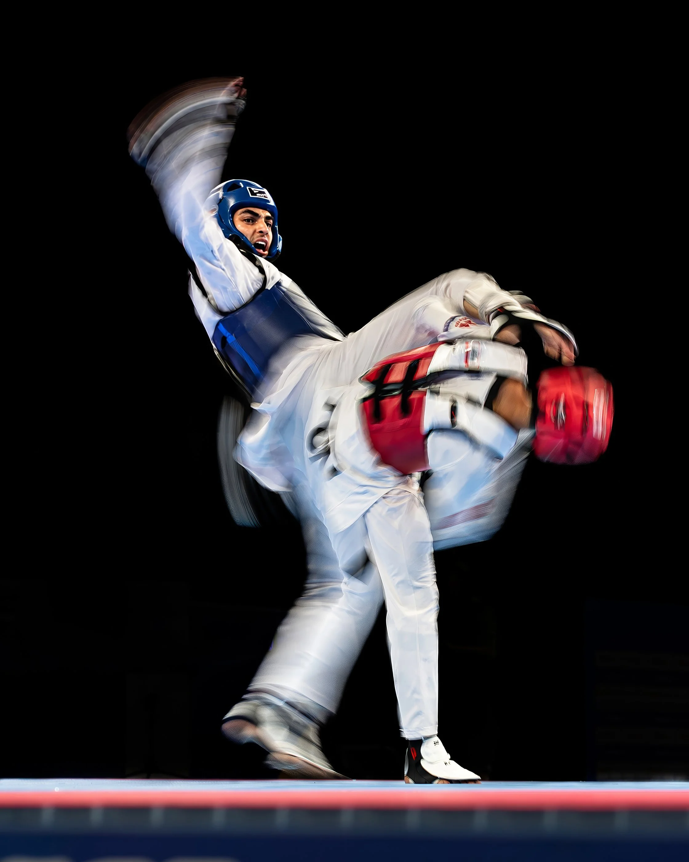 Athlete in taekwondo uniform executing a high kick during a match, with a focused expression, against a dark background.