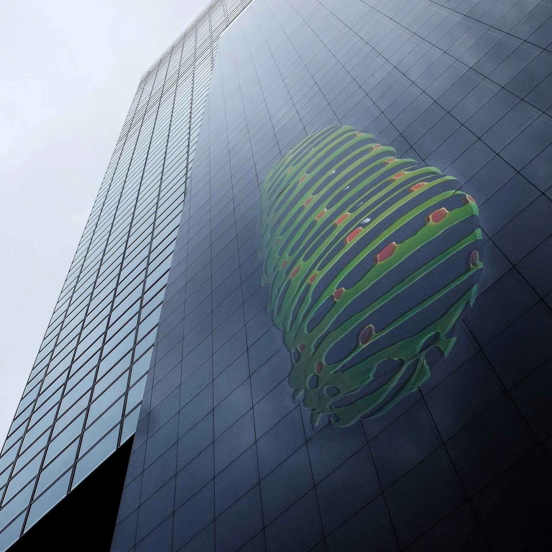 Reflection of a green and orange sculpture on a modern glass skyscraper