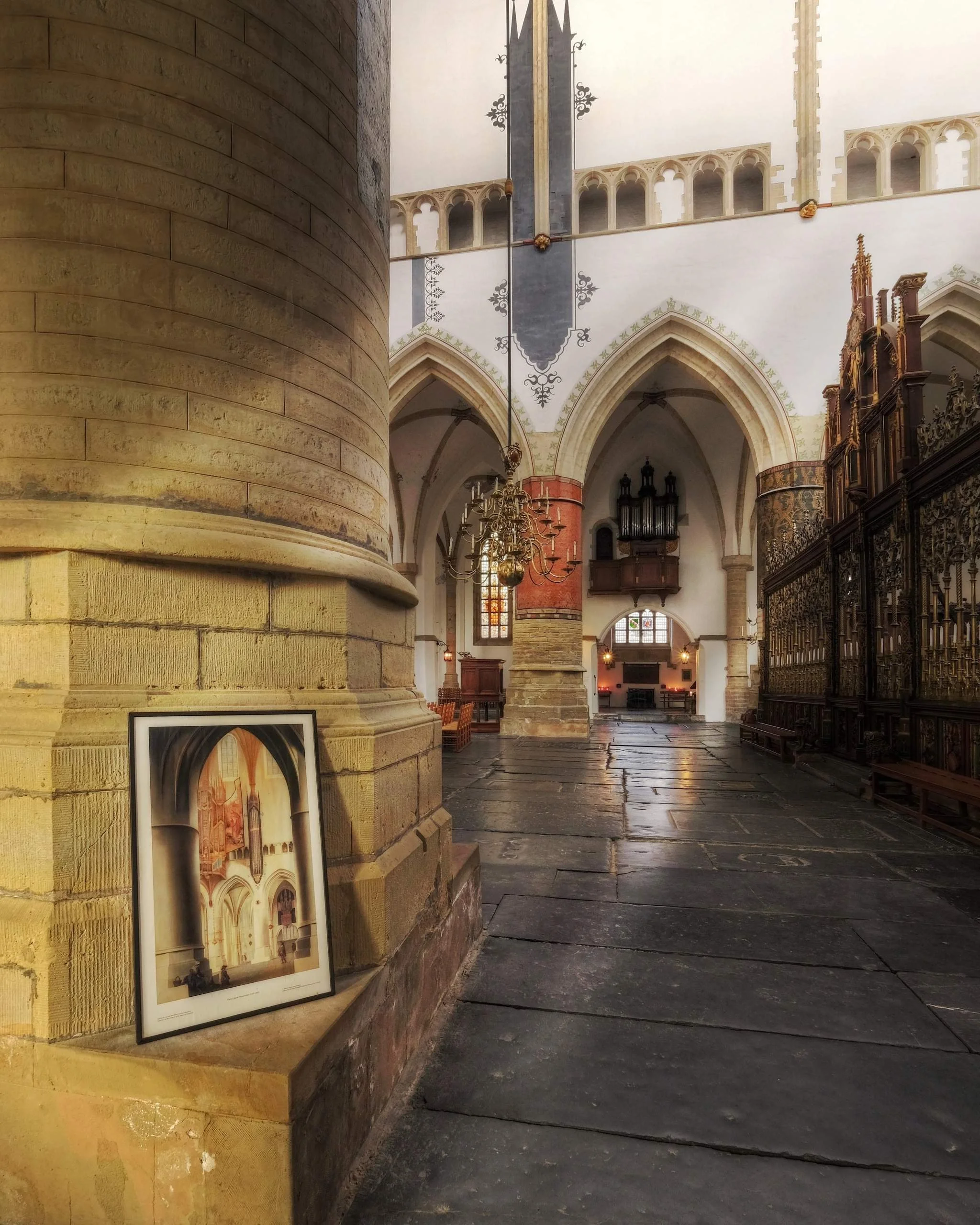 Interior of a historic church with stone columns, Gothic arches, chandeliers, and stained glass windows.