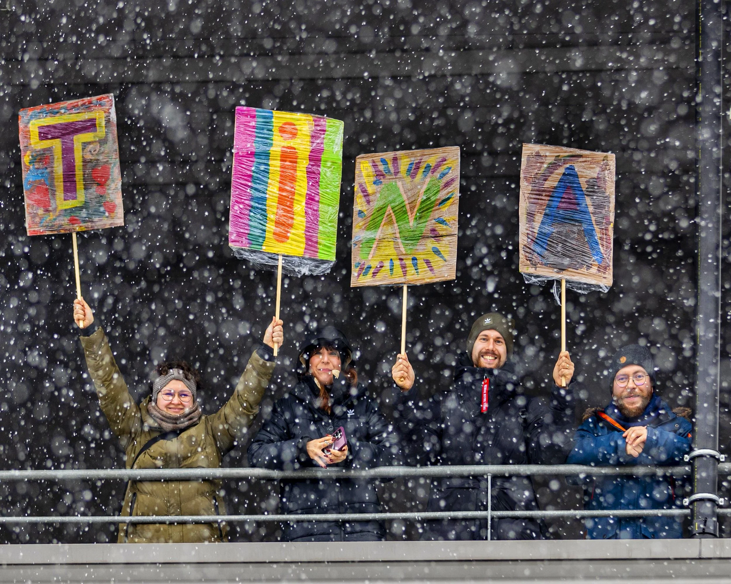Group of people holding colorful protest signs under snowfall.