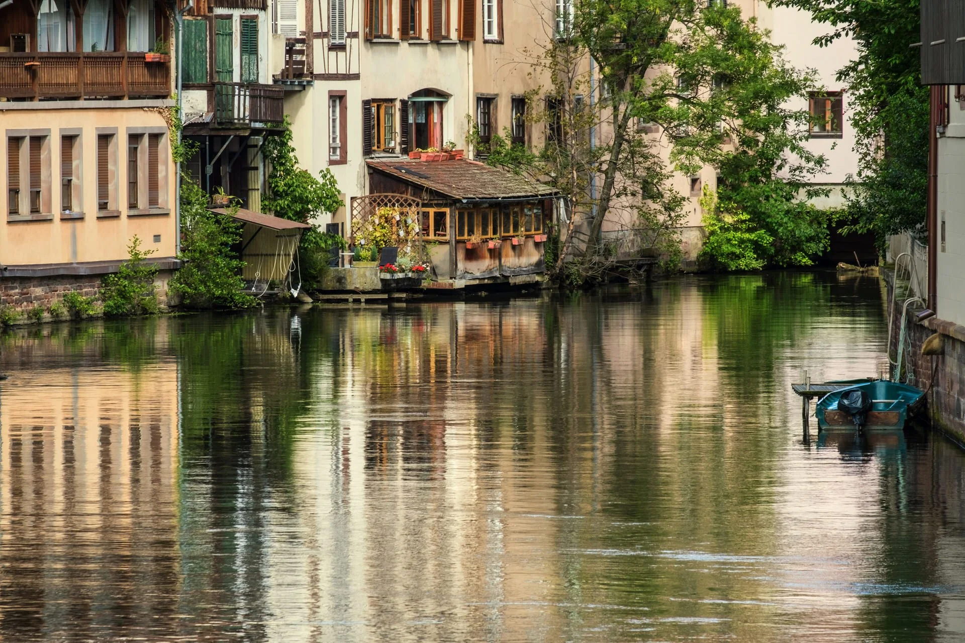 Waterfront buildings with open windows and a small dock with a boat next to the water.