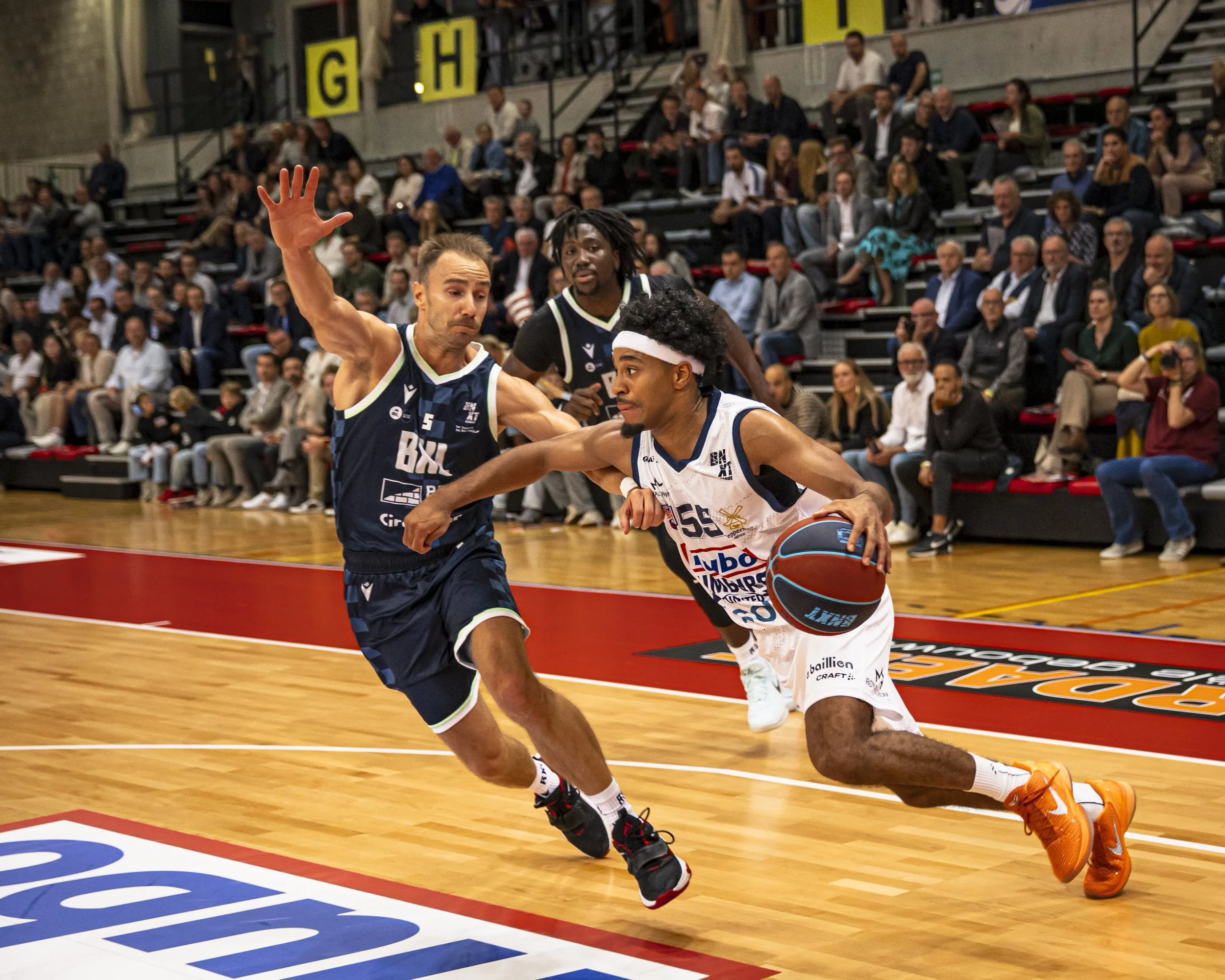Two basketball players competing for the ball during a game with spectators watching in the background.