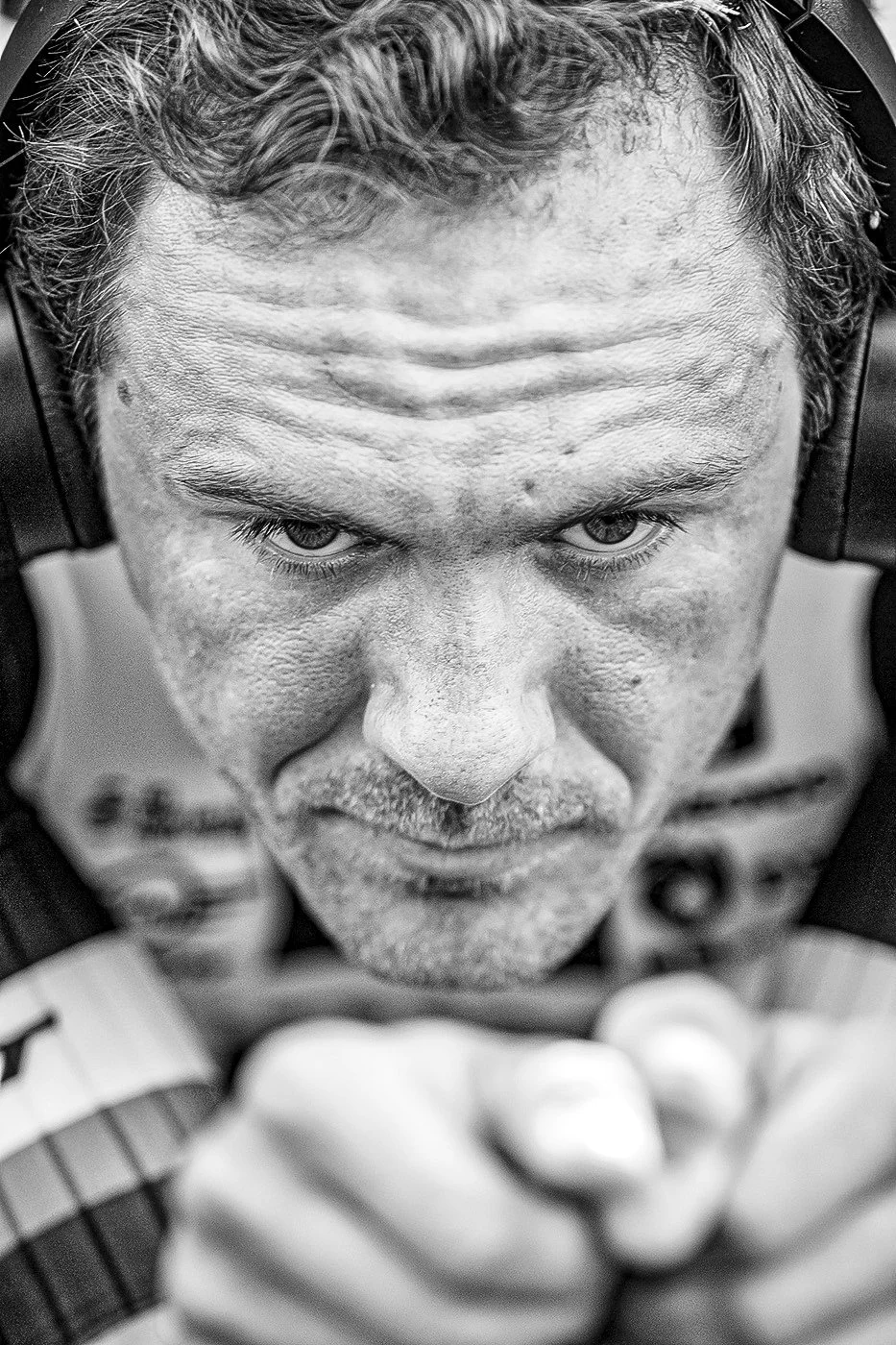 Close-up black and white photo of a man wearing headphones, looking intensely at the camera with a focused expression.