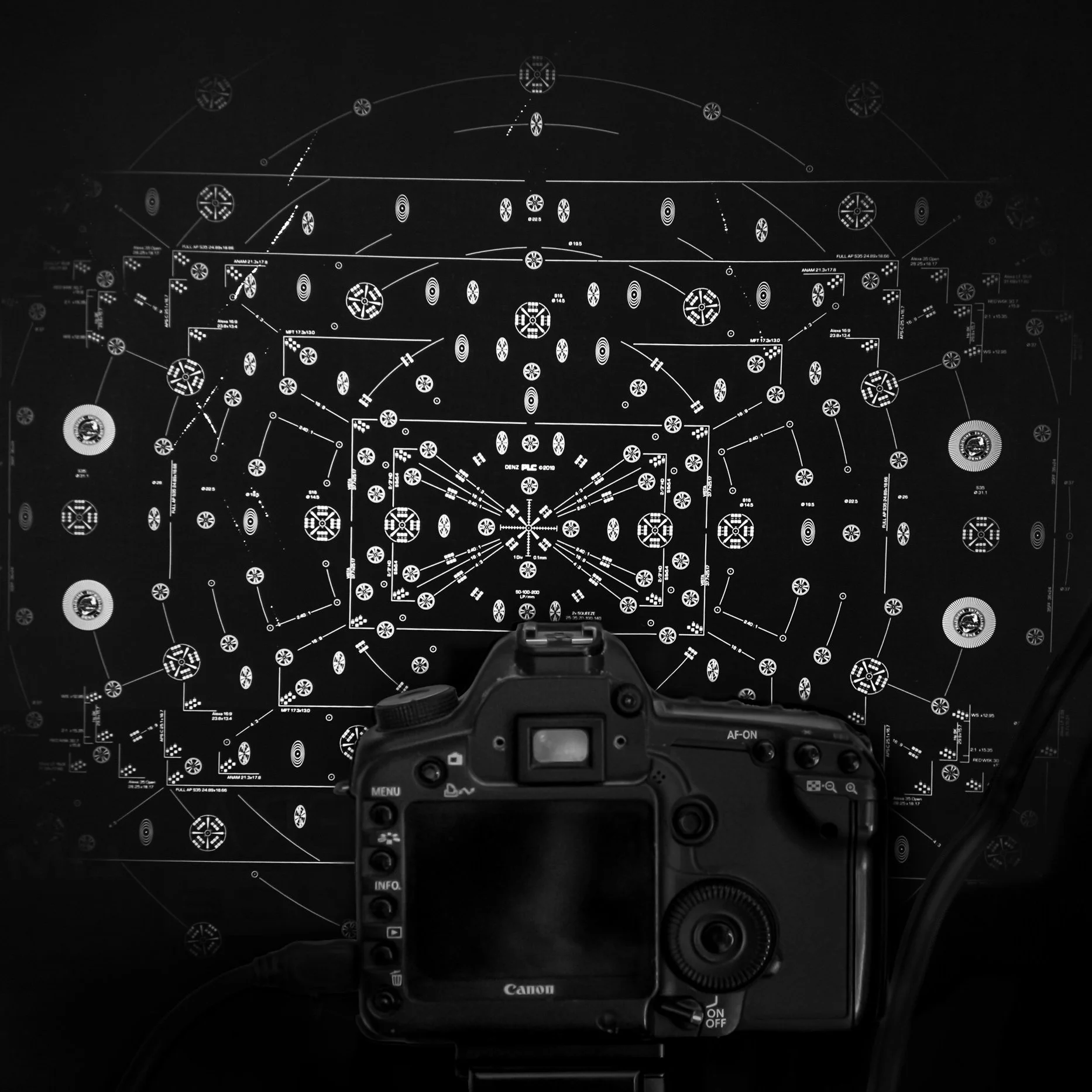 A computer monitor displaying a complex schematic diagram of technical symbols and connections, with a camera positioned in front capturing the image.