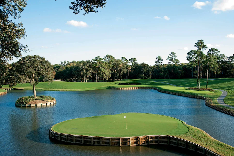 A golf course with a green surrounded by water, with trees and a clear sky in the background.