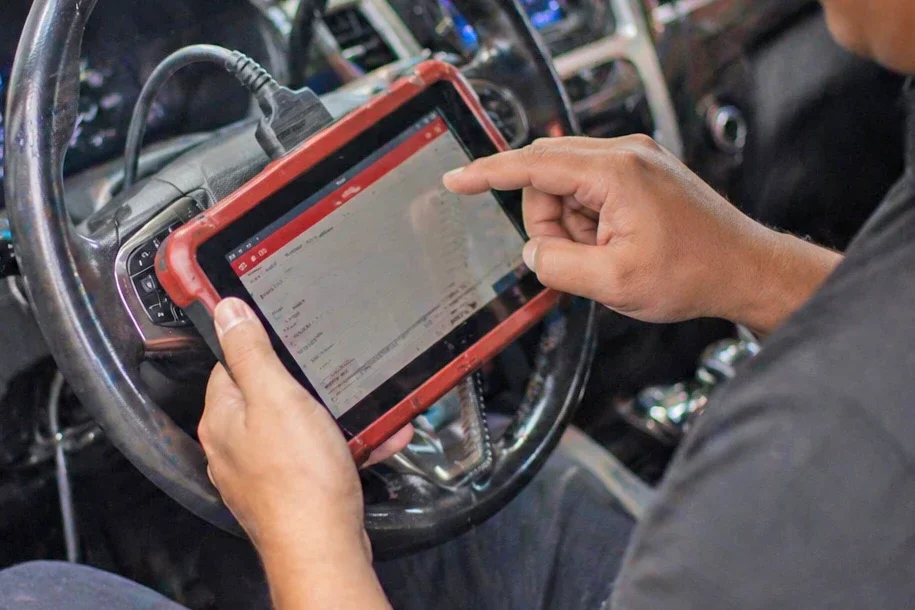 Person holding a tablet device with a red case inside a vehicle, using it on the steering wheel.