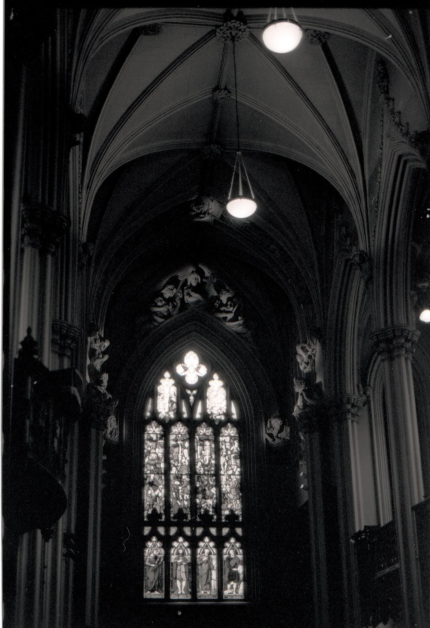 Interior view of a Gothic cathedral with arched ceilings, ornate carvings, and stained glass windows featuring religious figures.