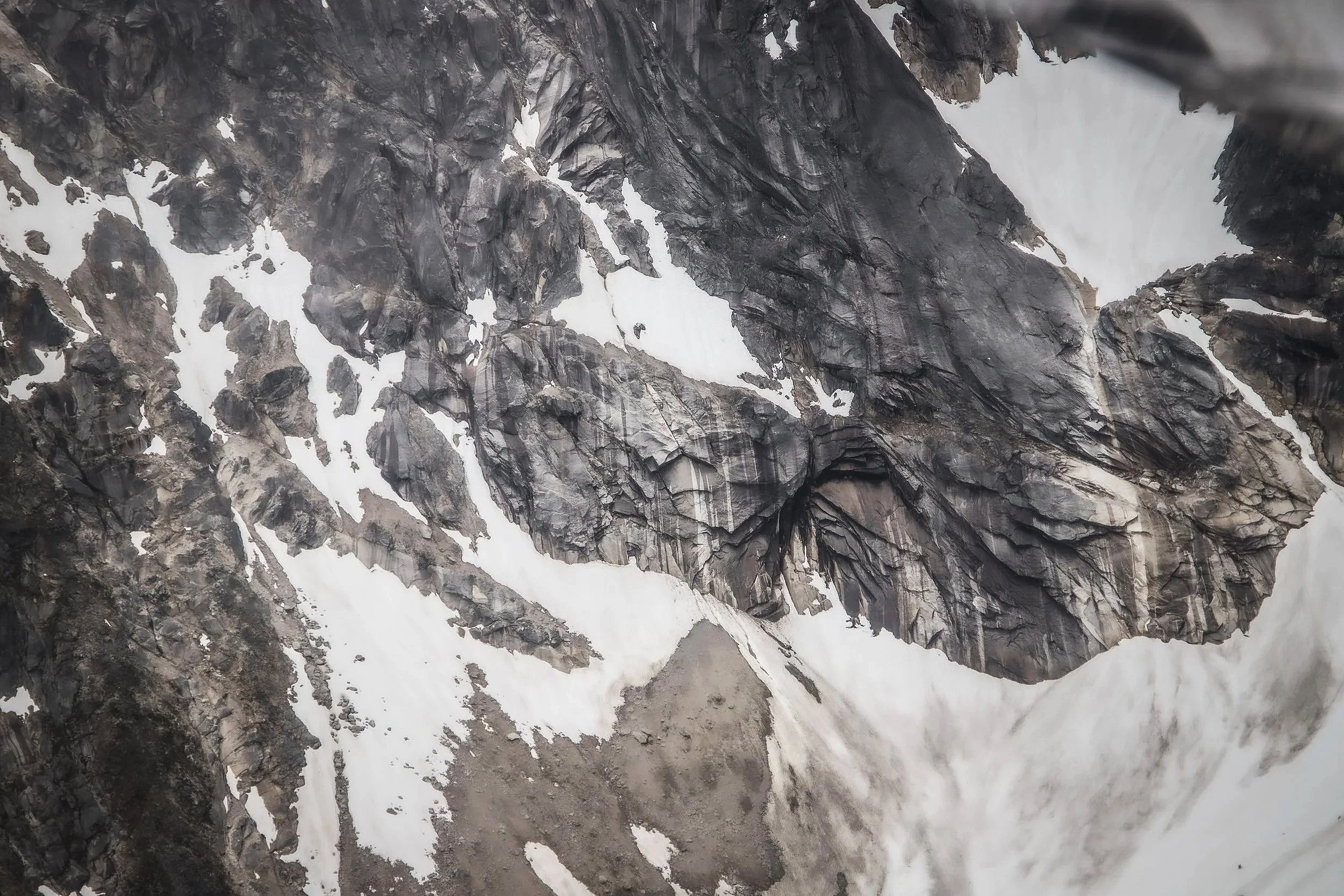 A rugged mountain slope with dark rocky formations and patches of snow.