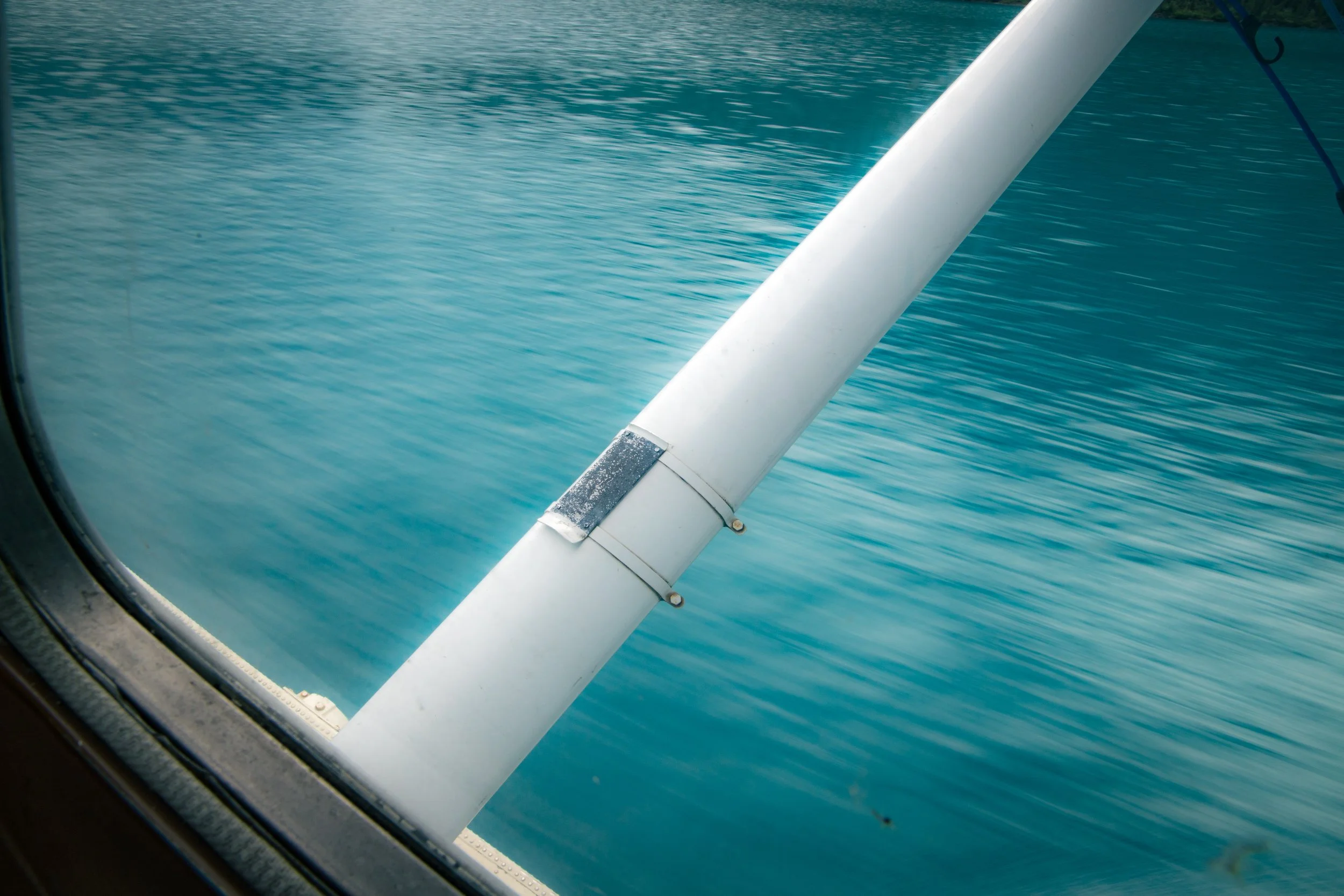 View through an airplane window showing part of the airplane's wing over a body of water.