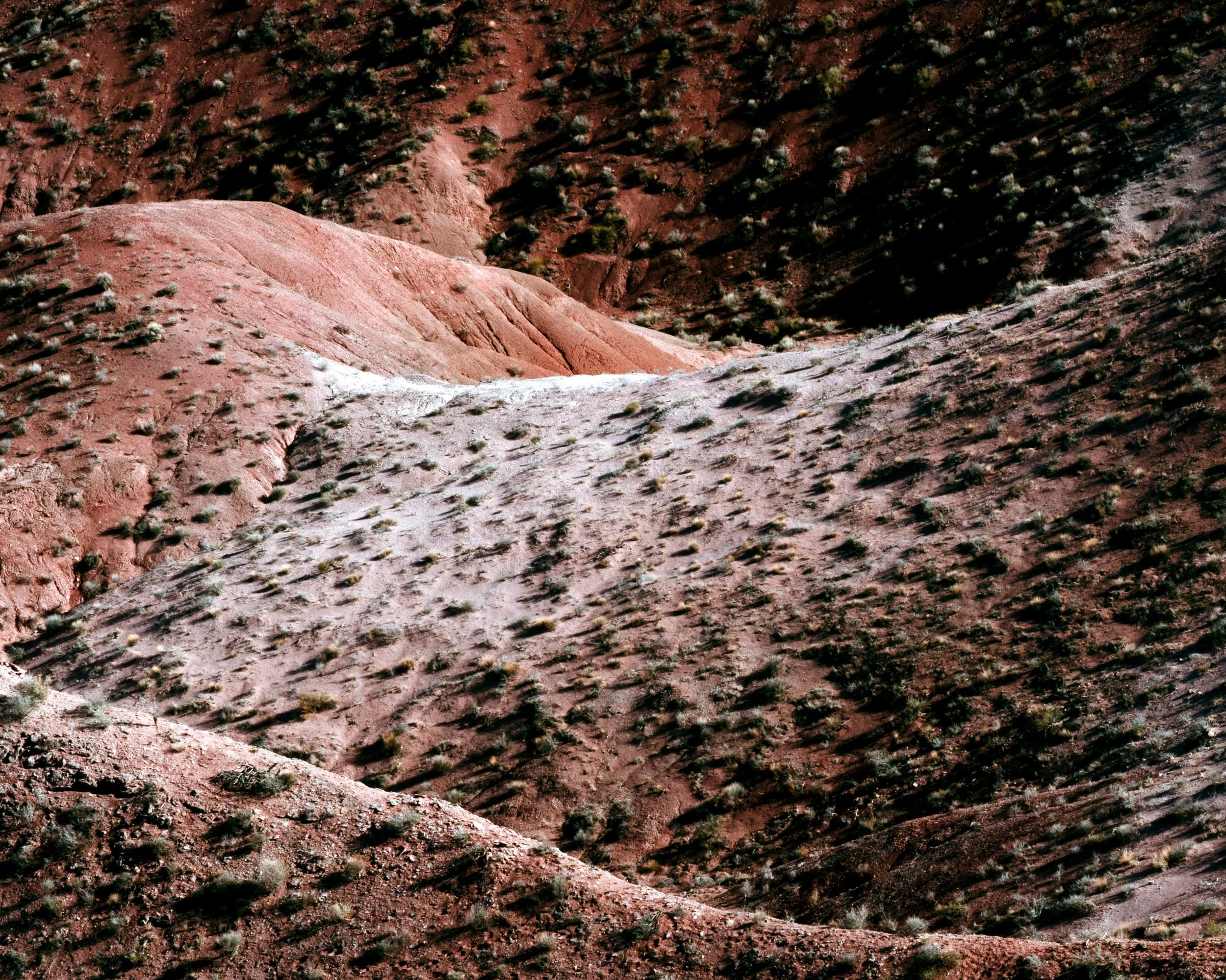 Aerial view of rugged, reddish desert terrain with sparse vegetation and small hills.