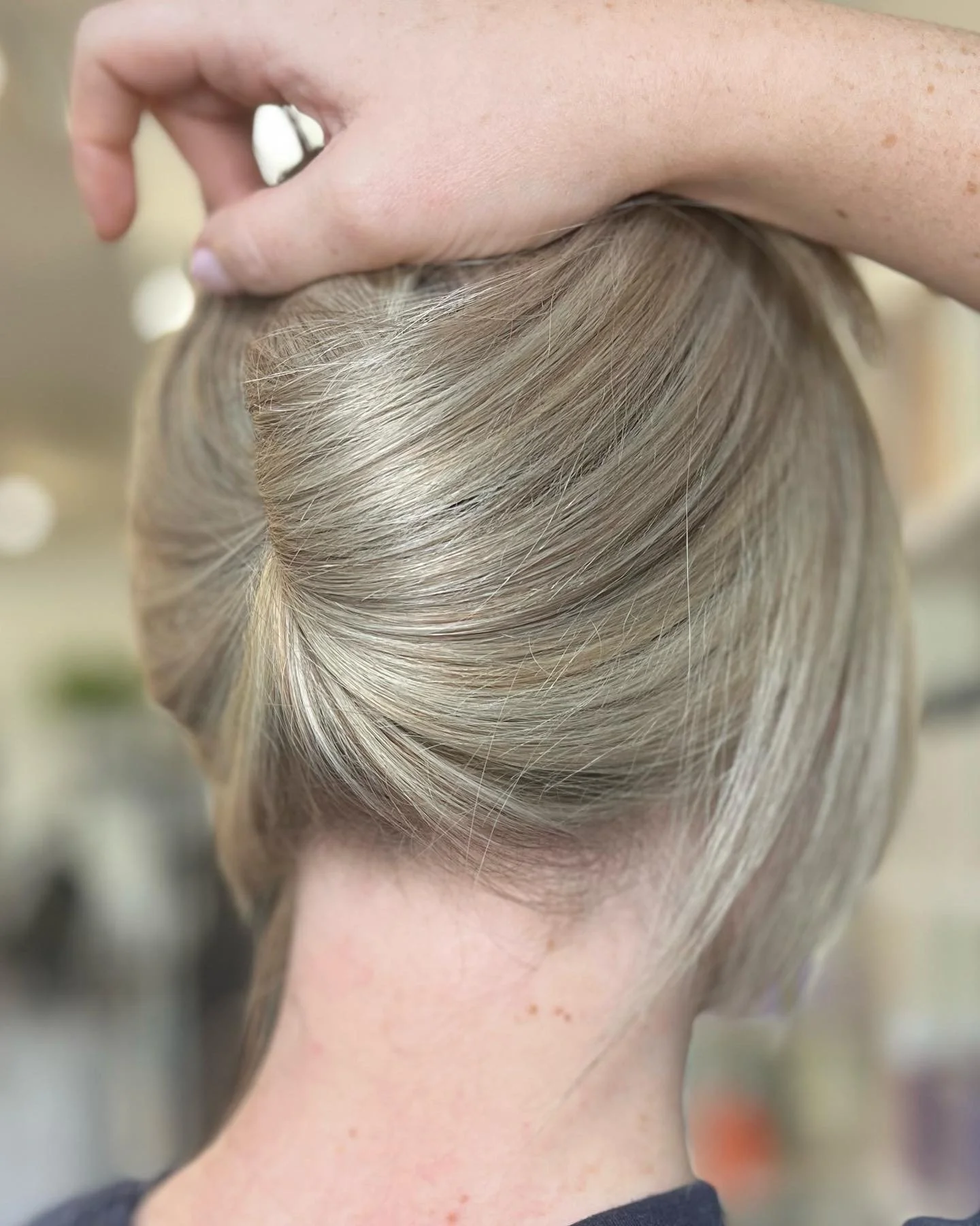 Close-up of a person with blonde hair styled in a rolled, vintage updo, with a hand on top of the head adjusting the hair.