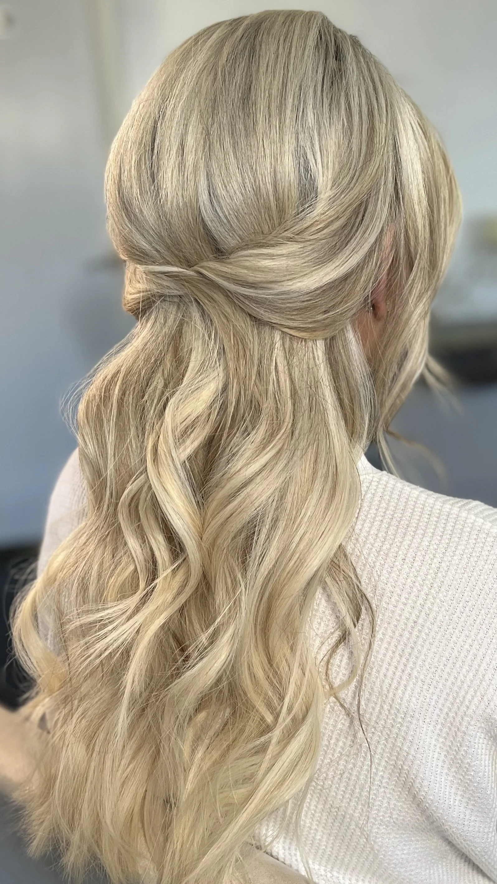 Blonde woman with long wavy hair, styled in loose curls, turned slightly away from the camera.